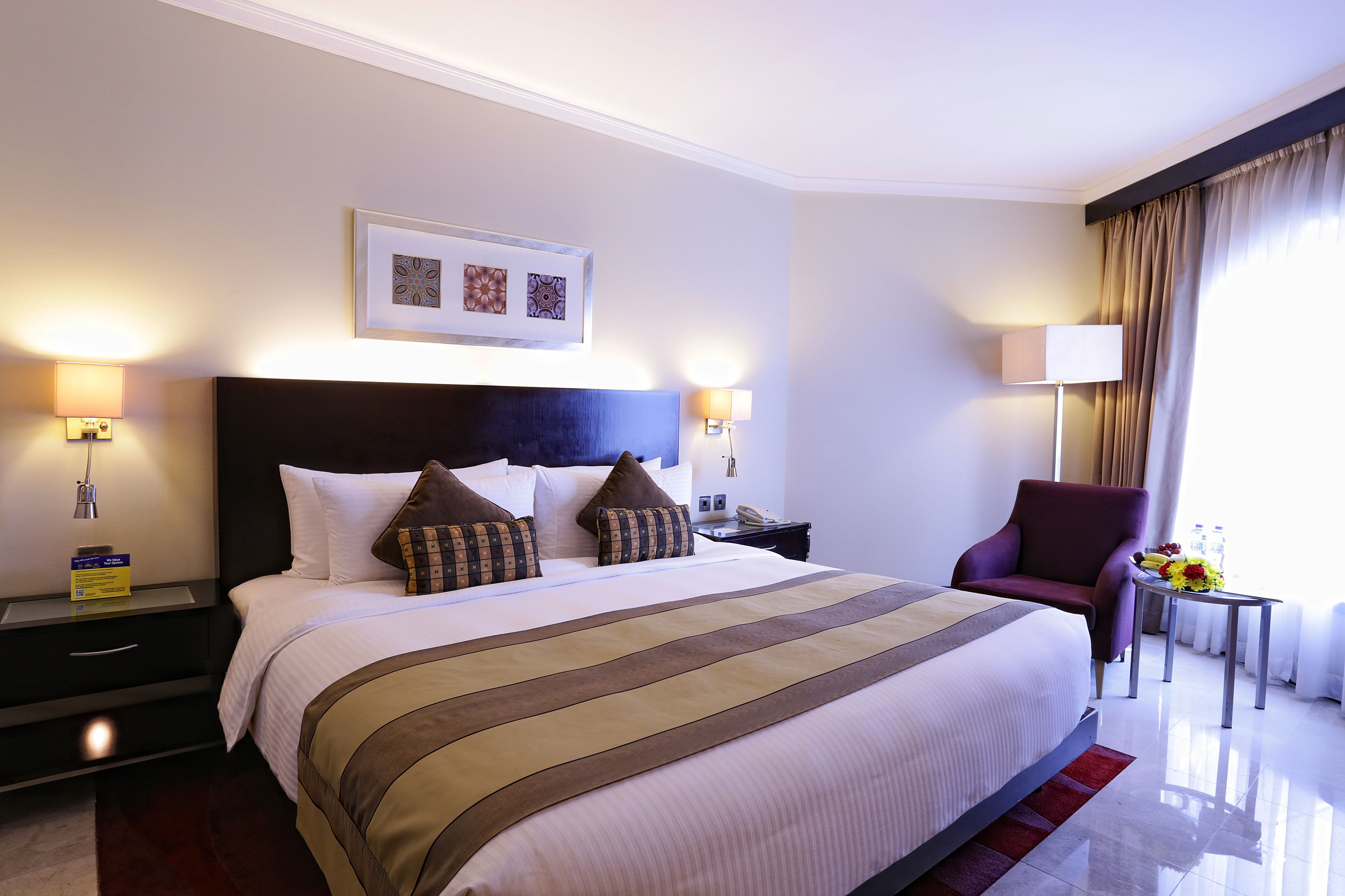 Una habitación de hotel con una cama grande, dos mesitas de noche, una silla, una pequeña mesa con flores y una ventana con cortinas.