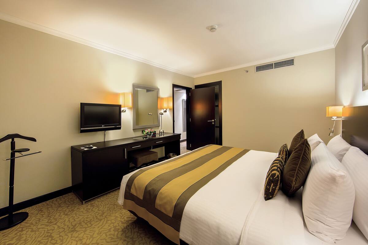 A hotel room with a bed, a desk, a television, and a door.