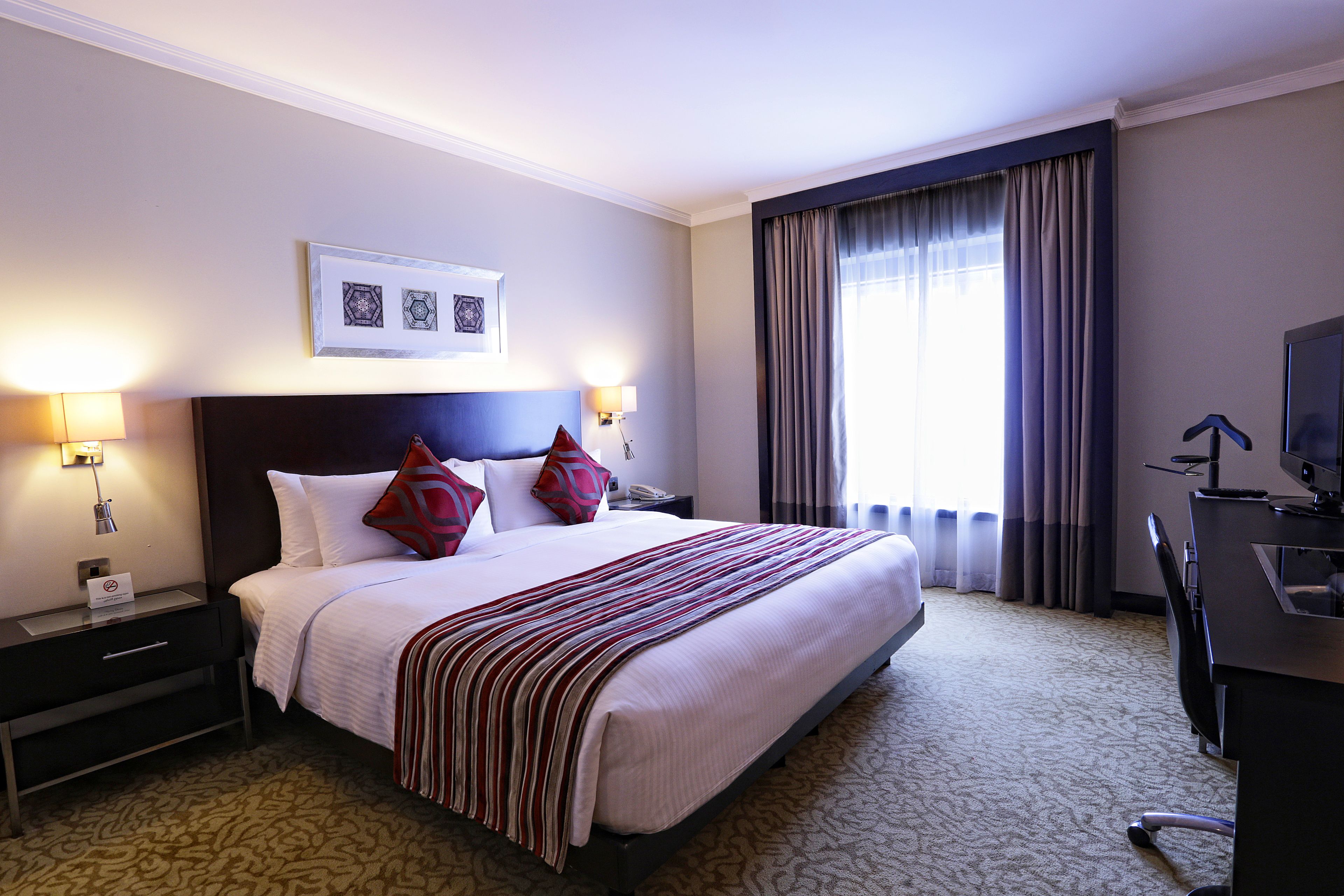 A hotel room with a large bed, two bedside lamps, a desk with a chair, and a TV.