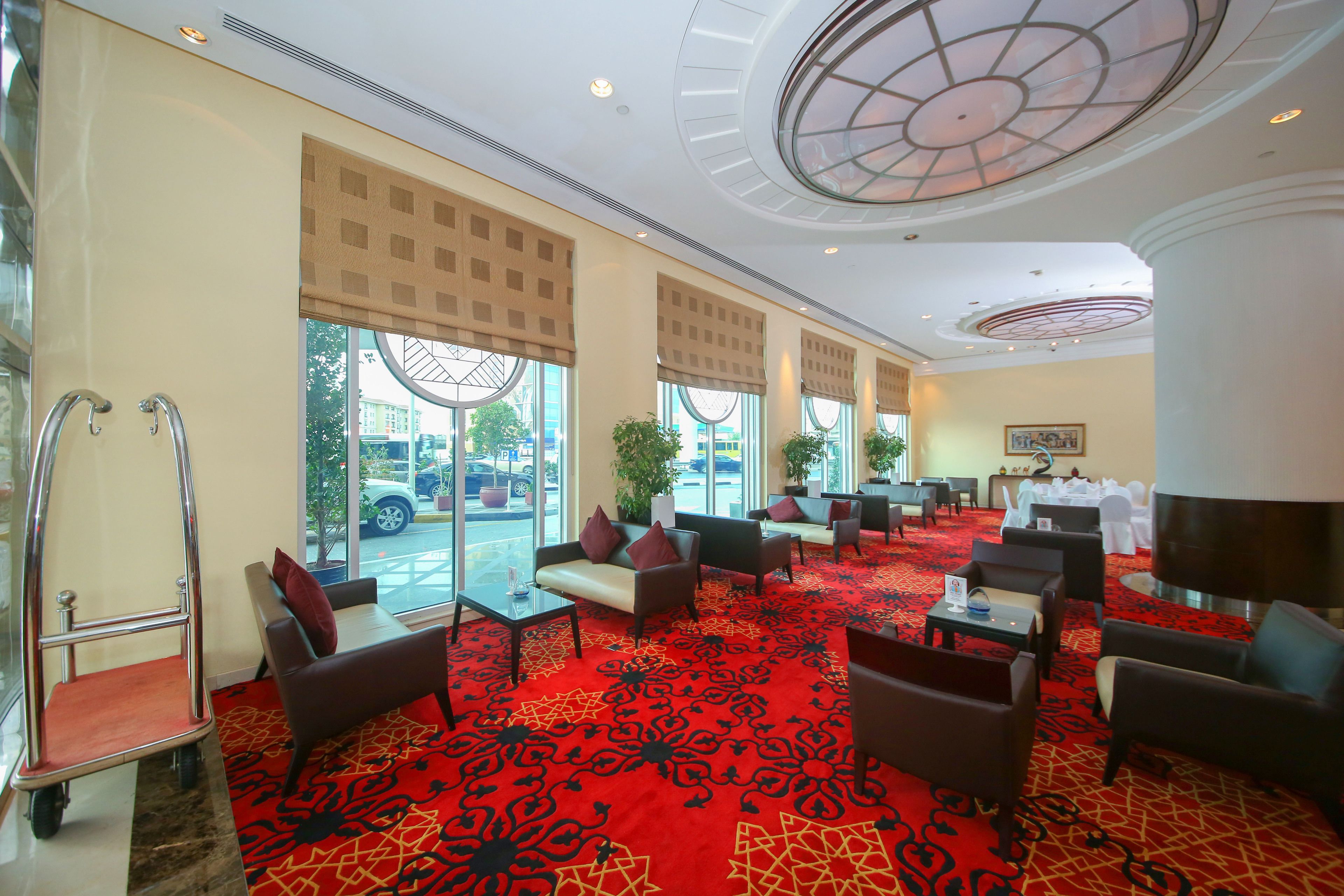 Un hall de hotel con alfombra roja estampada, zonas de estar y grandes ventanales.