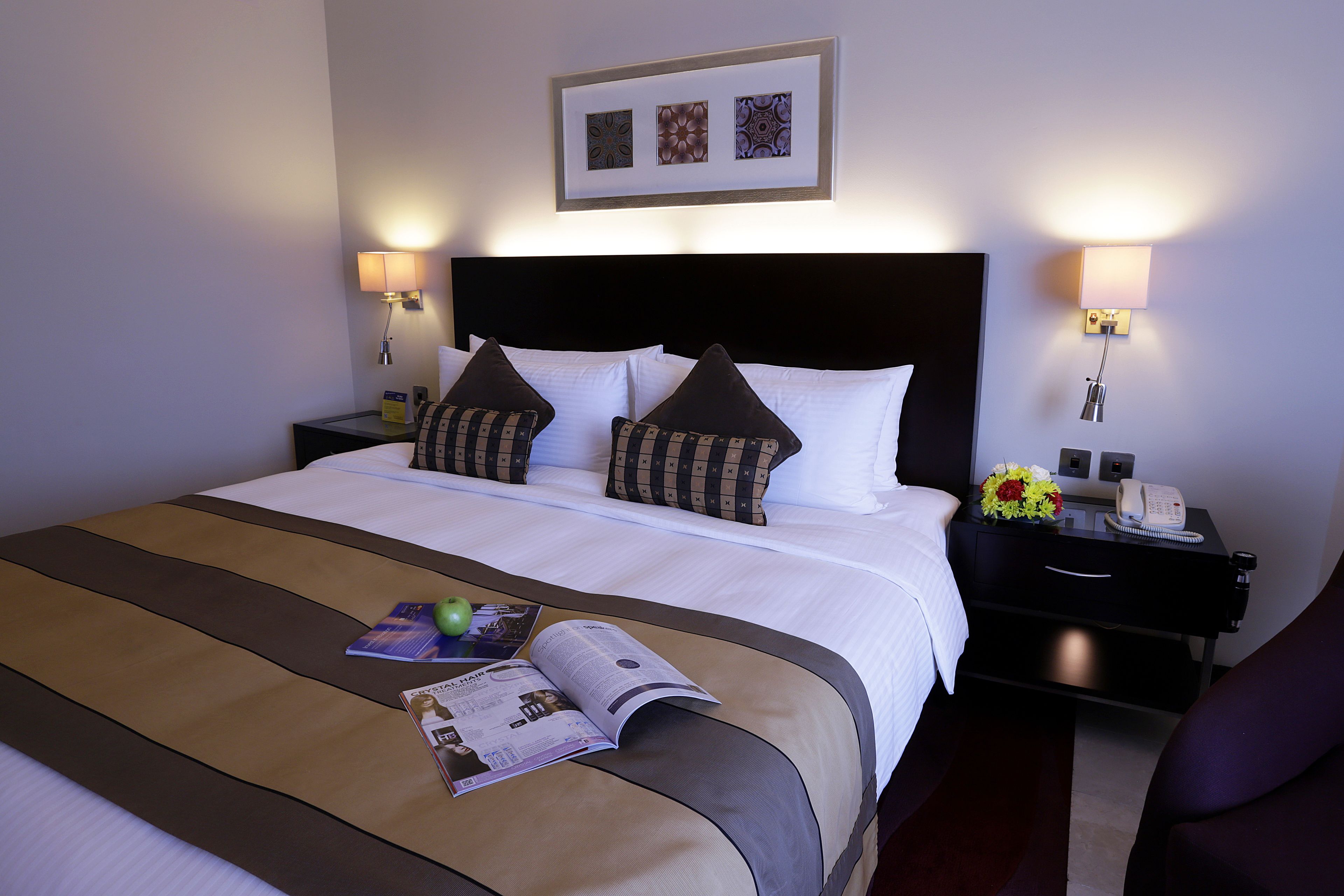 Una habitación de hotel con una cama bien hecha, una mesita de noche con una lámpara, un teléfono y un jarrón con flores.