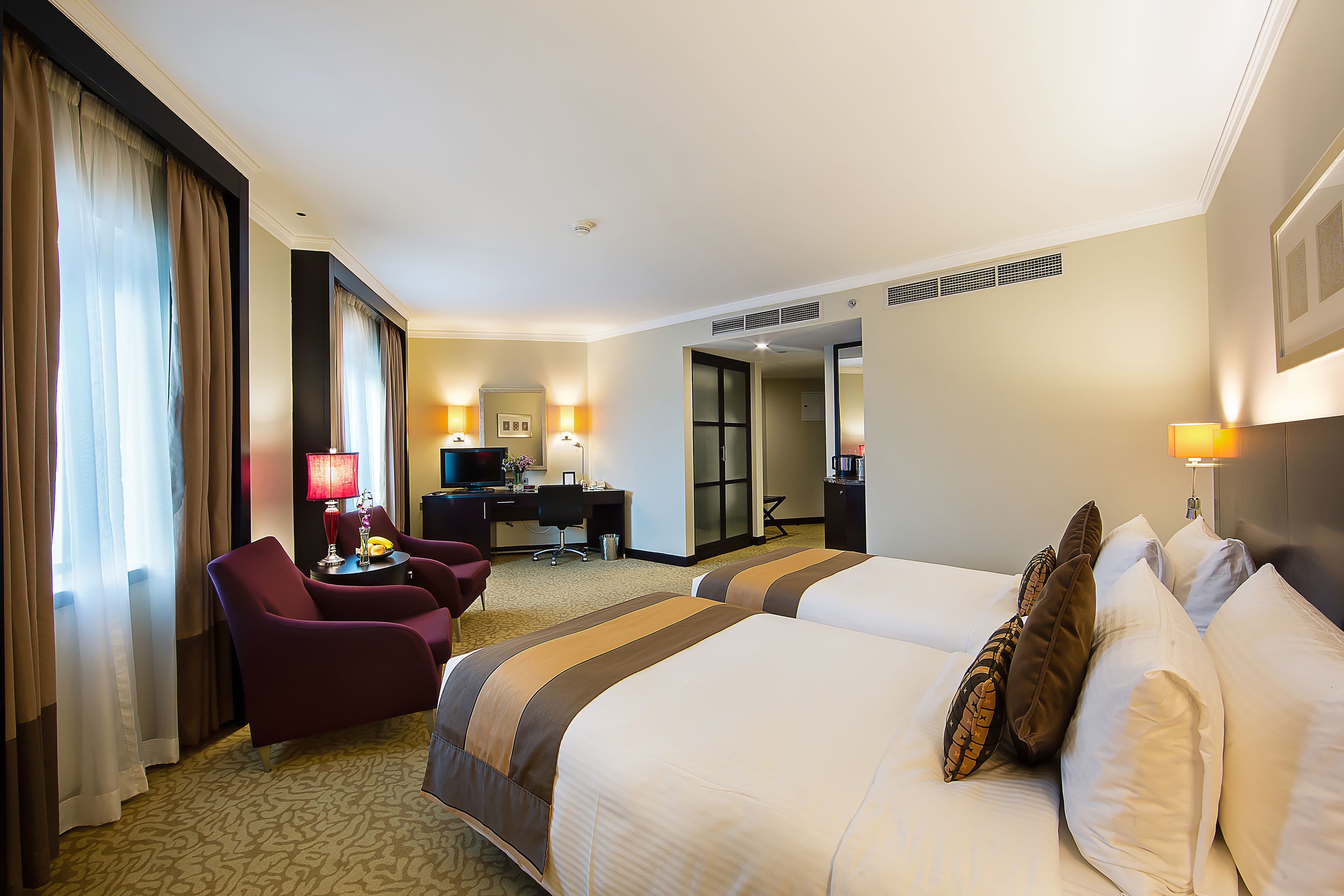 A hotel room with two beds, a desk, a chair, and a desk lamp.