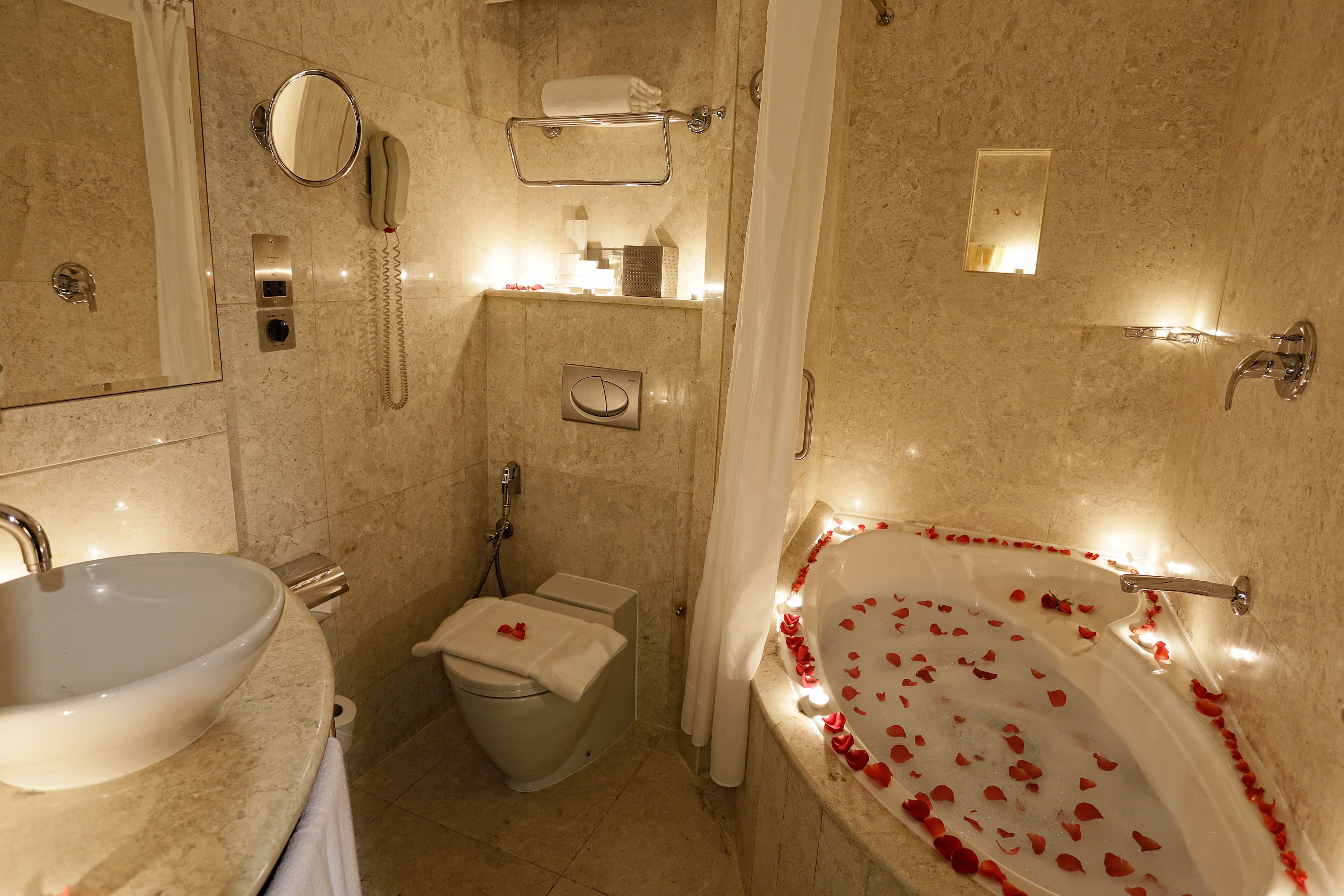 Un baño con lavamanos, inodoro y bañera con pétalos de rosa.