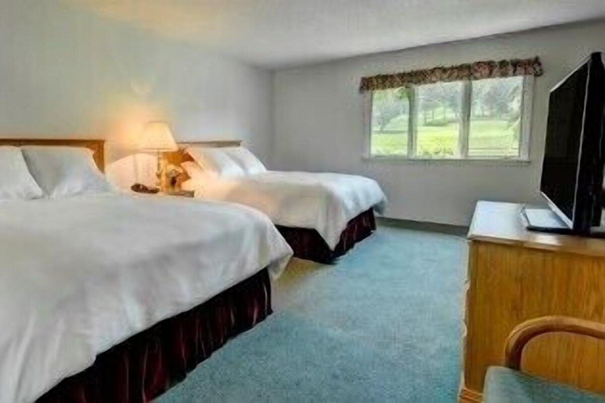 A hotel room with two beds, a desk, and a television.