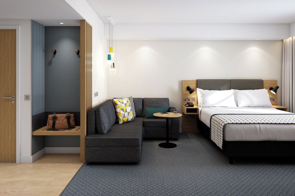 A modern hotel room with a sofa, a bed, a small table, and a nightstand.