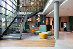 A modern interior with a staircase, seating area, and a large pillar. - Holiday Inn Ratingen City by IHG (Ratingen)