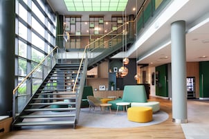 A modern interior with a staircase, seating areas, and a high ceiling with skylights.