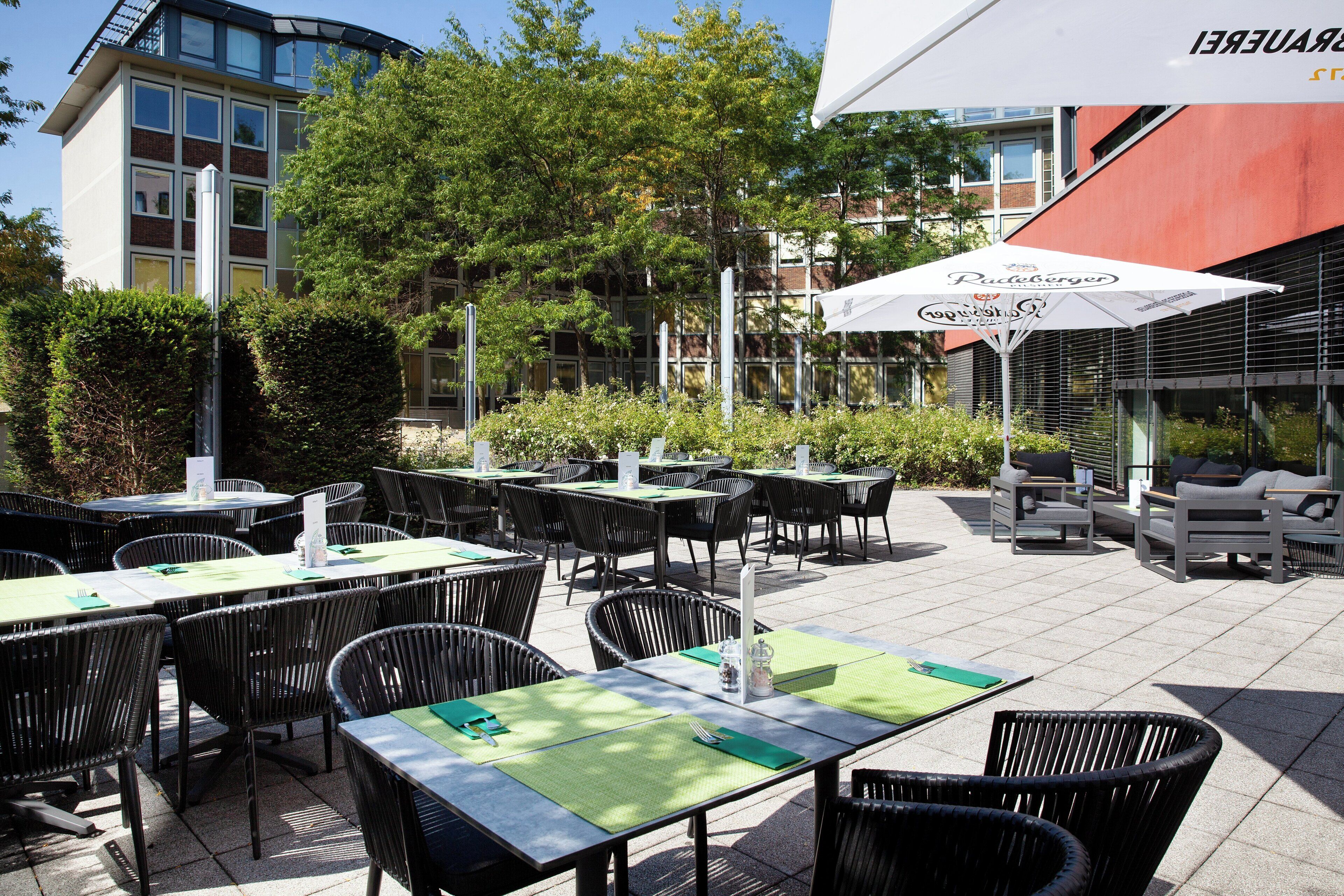 An outdoor seating area with tables and chairs, a covered umbrella, and a building in the background.