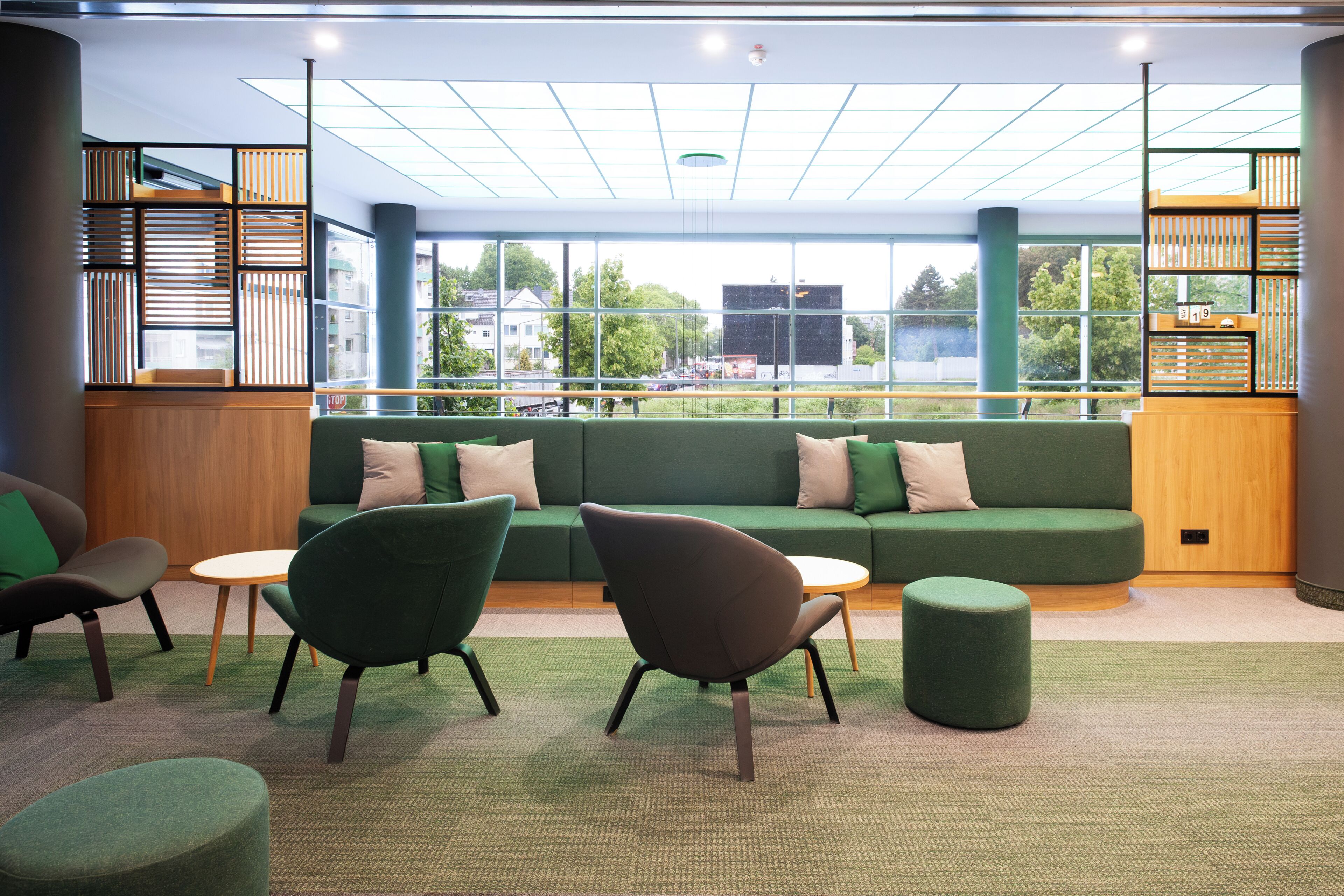 A modern lounge area with a green sofa, two armchairs, a small table, and a green ottoman.