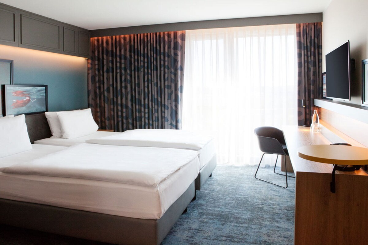 A hotel room with a large bed, a desk with a chair, a television, and a window with curtains.