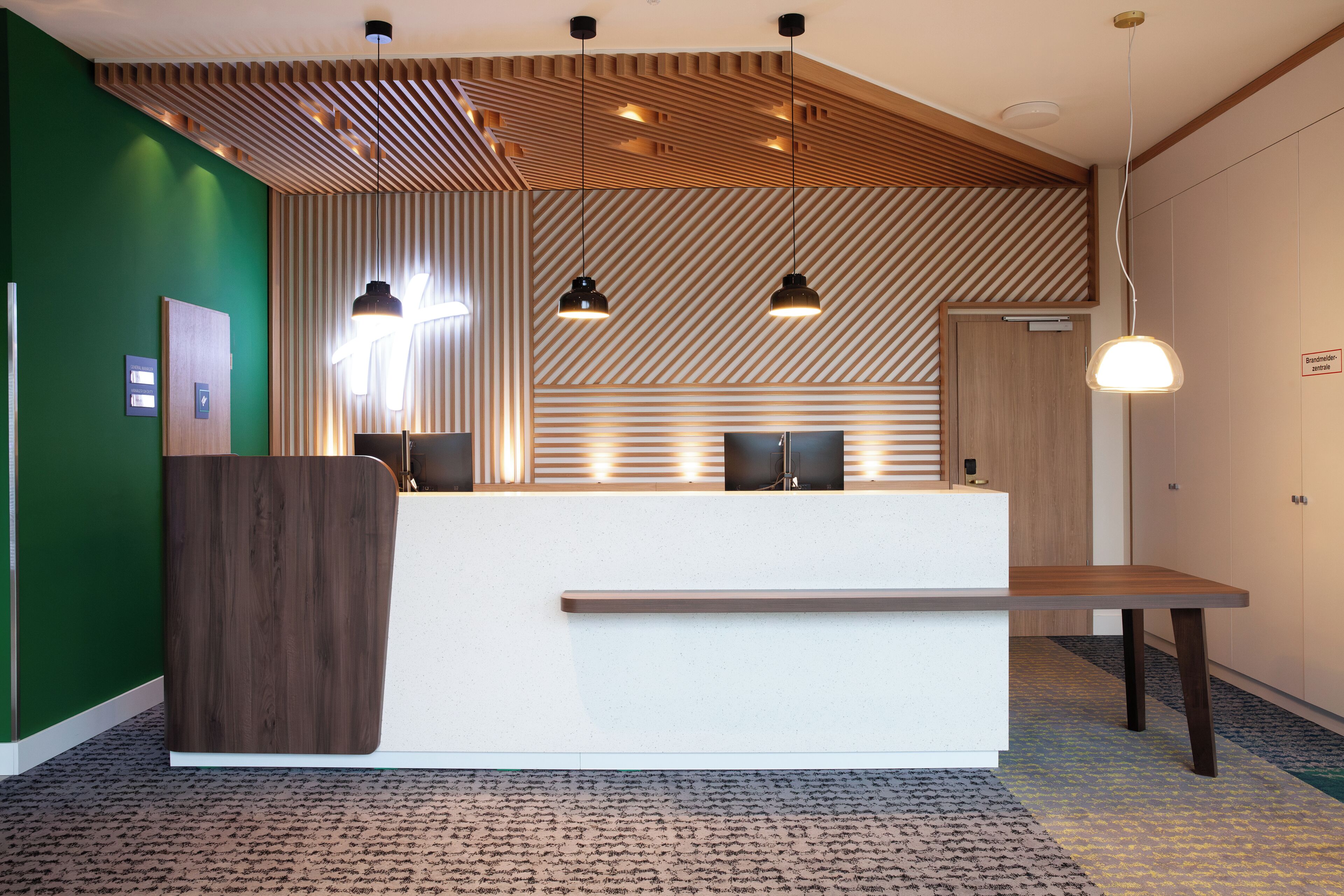 A reception desk with a wooden panel wall, pendant lighting, and a patterned carpet.