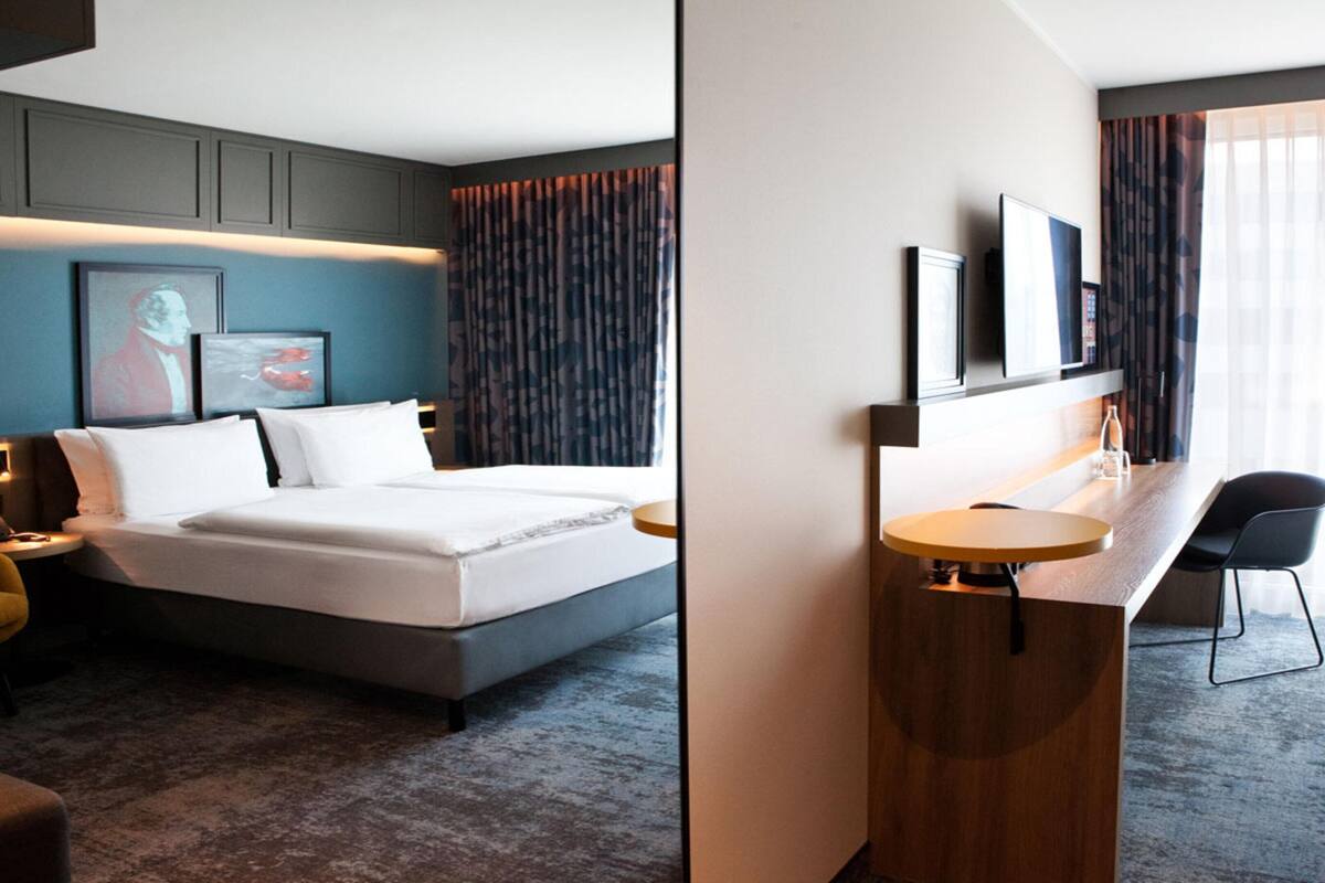 A hotel room with a bed, a desk, a chair, a TV, and a window with curtains.