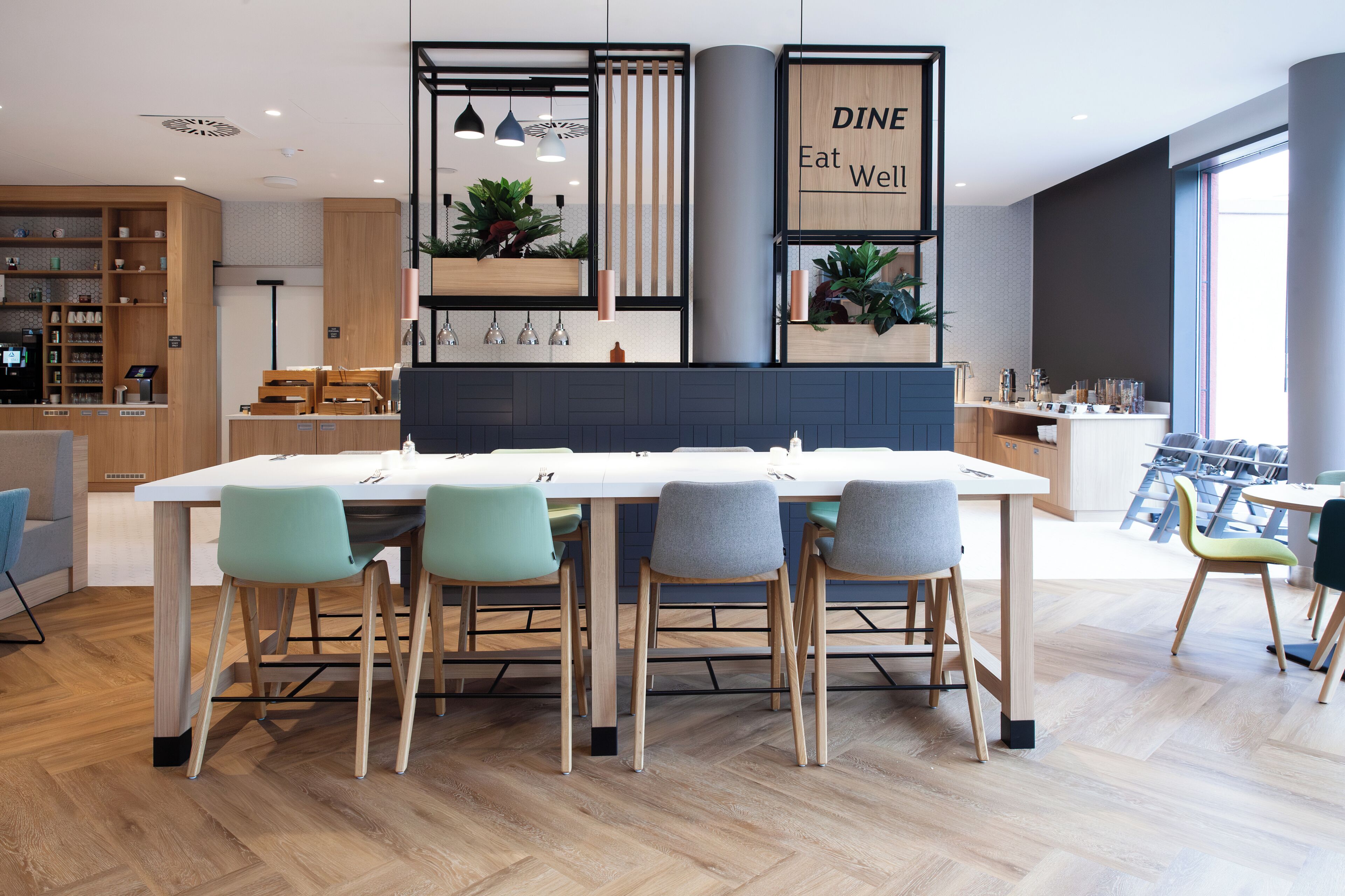 A modern dining area with a long table, four chairs, and a sign that reads 'DINE Eat Well'.