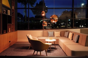 A modern living room with a sectional sofa, a yellow armchair, and a small round table. - Holiday Inn Ratingen City by IHG (Ratingen)