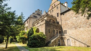 Un bâtiment historique en pierre, doté d’un escalier central, de fenêtres en arc de cercle et d’une tour.