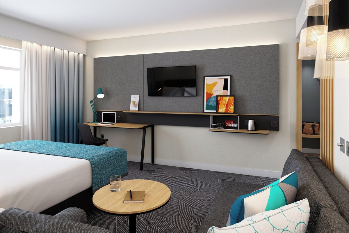 A hotel room with a bed, a desk, a TV, a sofa, and a small table.