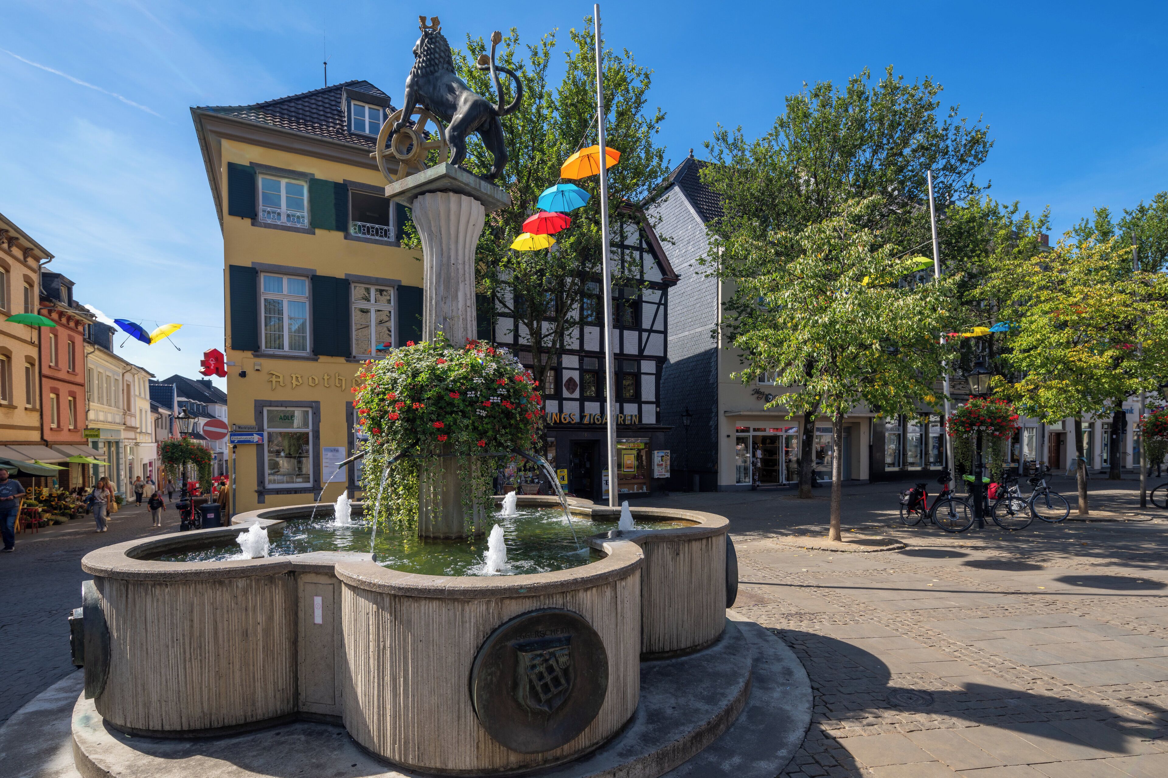 A public square with a fountain, a statue, and surrounding buildings.