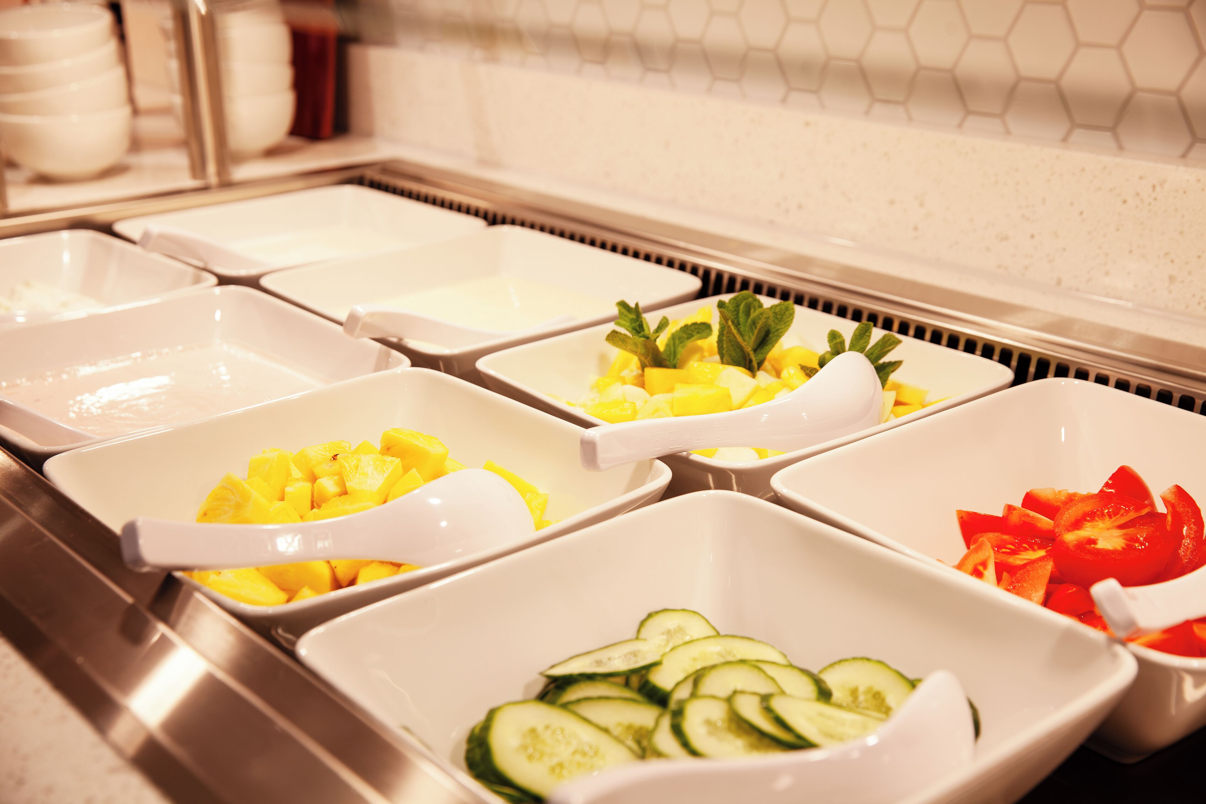 A buffet with various food items in white bowls, including fruits and vegetables.