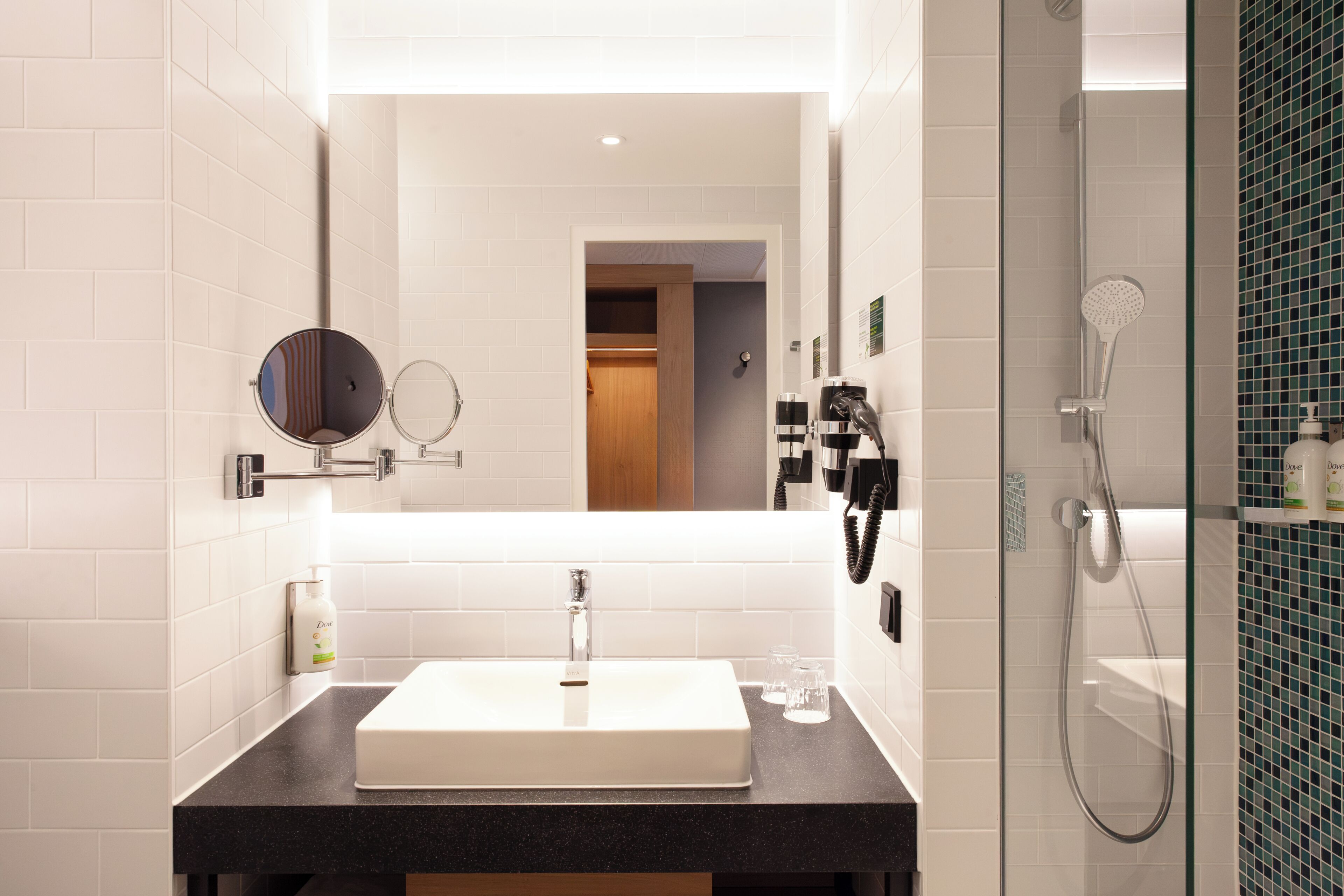 A modern bathroom with a white sink, a round mirror, a handheld showerhead, and a glass-enclosed shower.