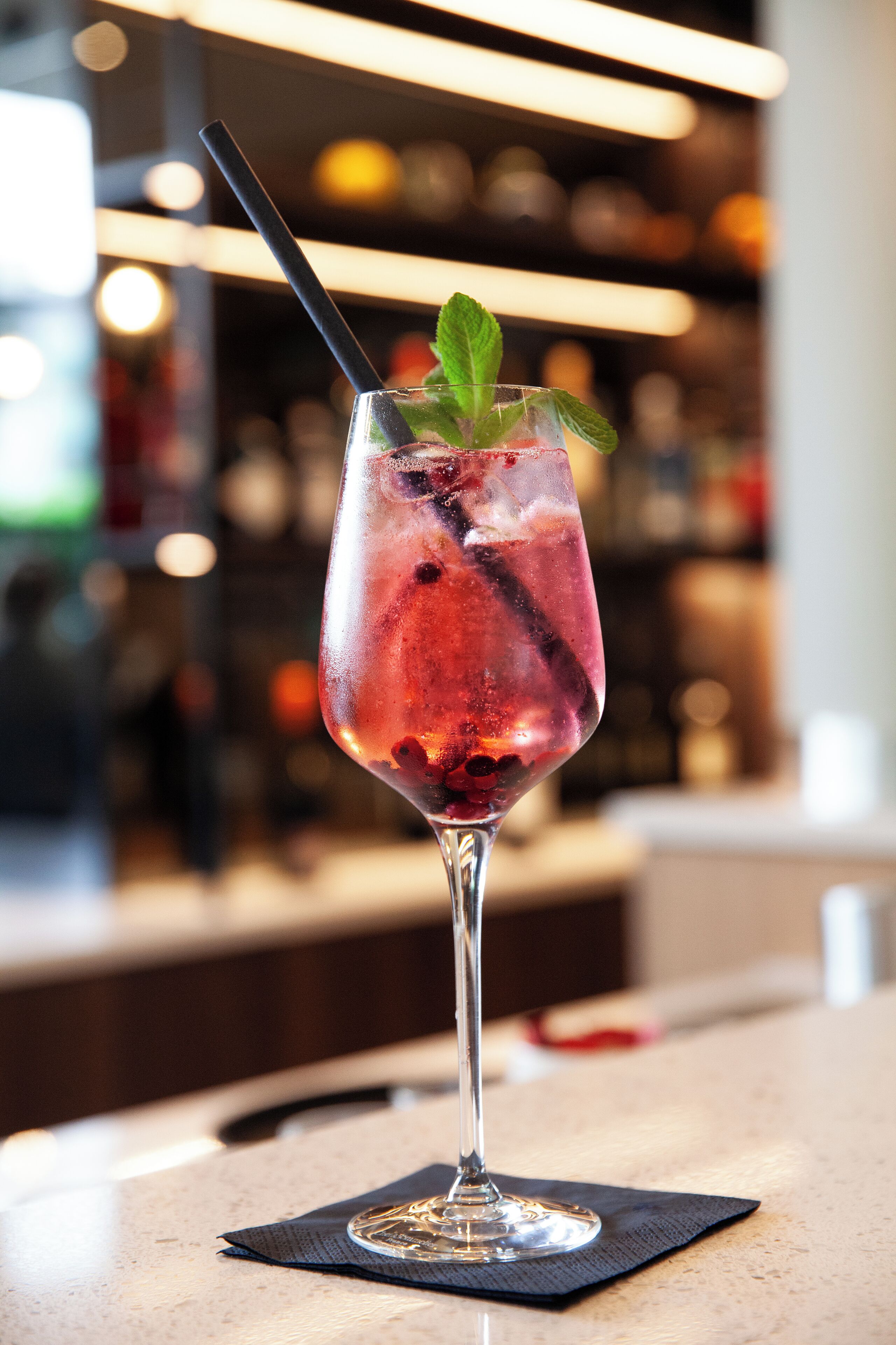 A cocktail glass with a straw and mint garnish on a bar counter.