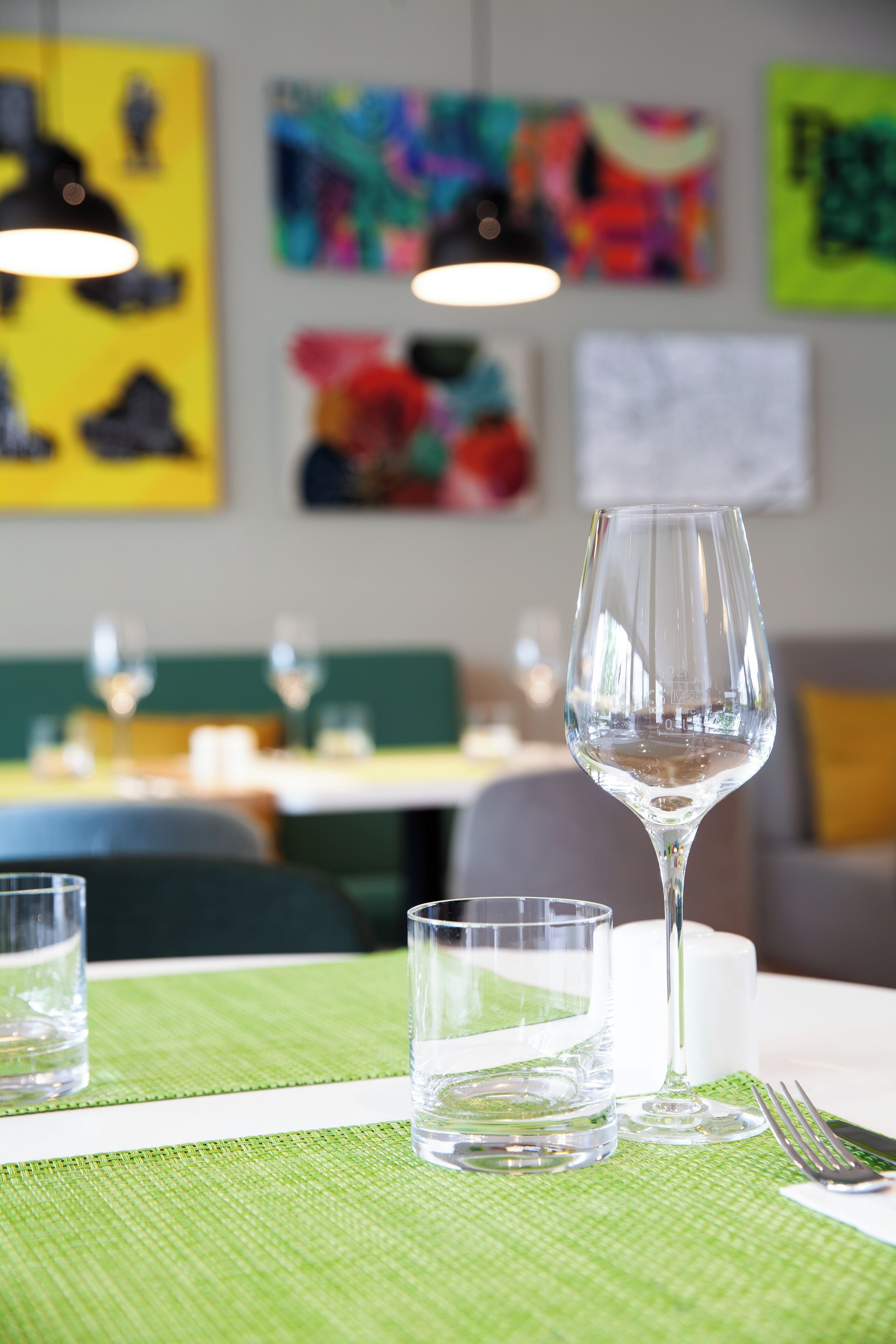 A dining table with a wine glass, a water glass, and a fork on a green placemat.