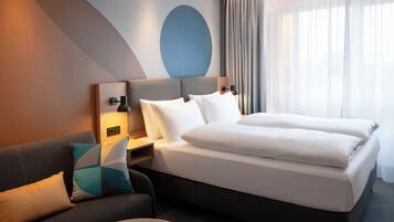 A hotel room with a bed, a sofa, a nightstand, and a wall with a geometric design.
