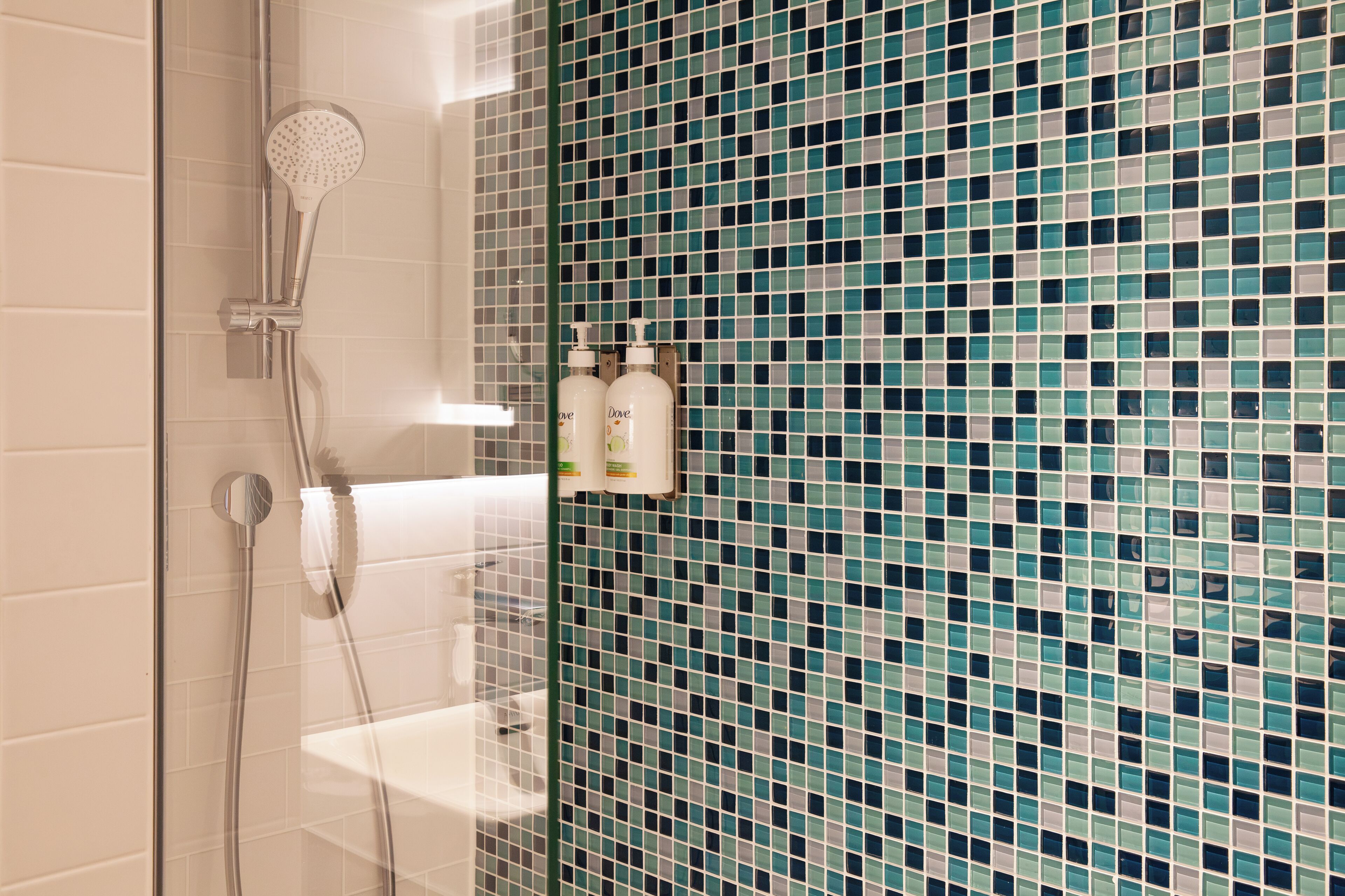 A bathroom with a shower, a glass door, and a tiled wall.