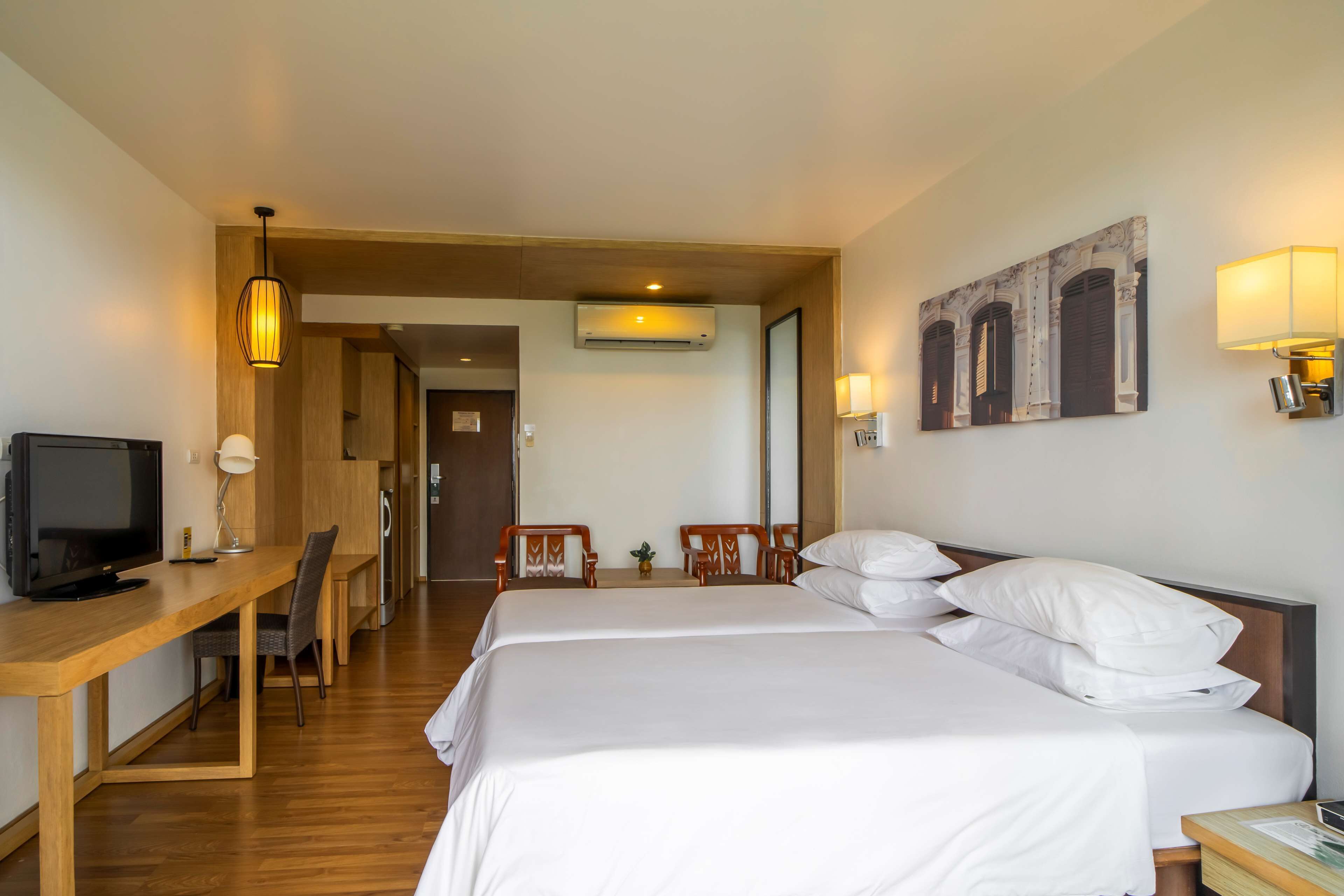 A hotel room with two beds, a desk with a television, a chair, and a lamp.