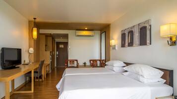 A hotel room with two beds, a desk with a television, a chair, and a lamp.