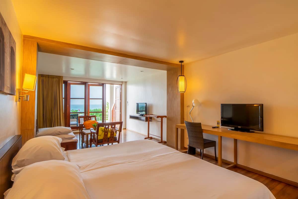 Habitación de hotel con una cama grande, un escritorio con televisión, una silla y vistas al exterior.