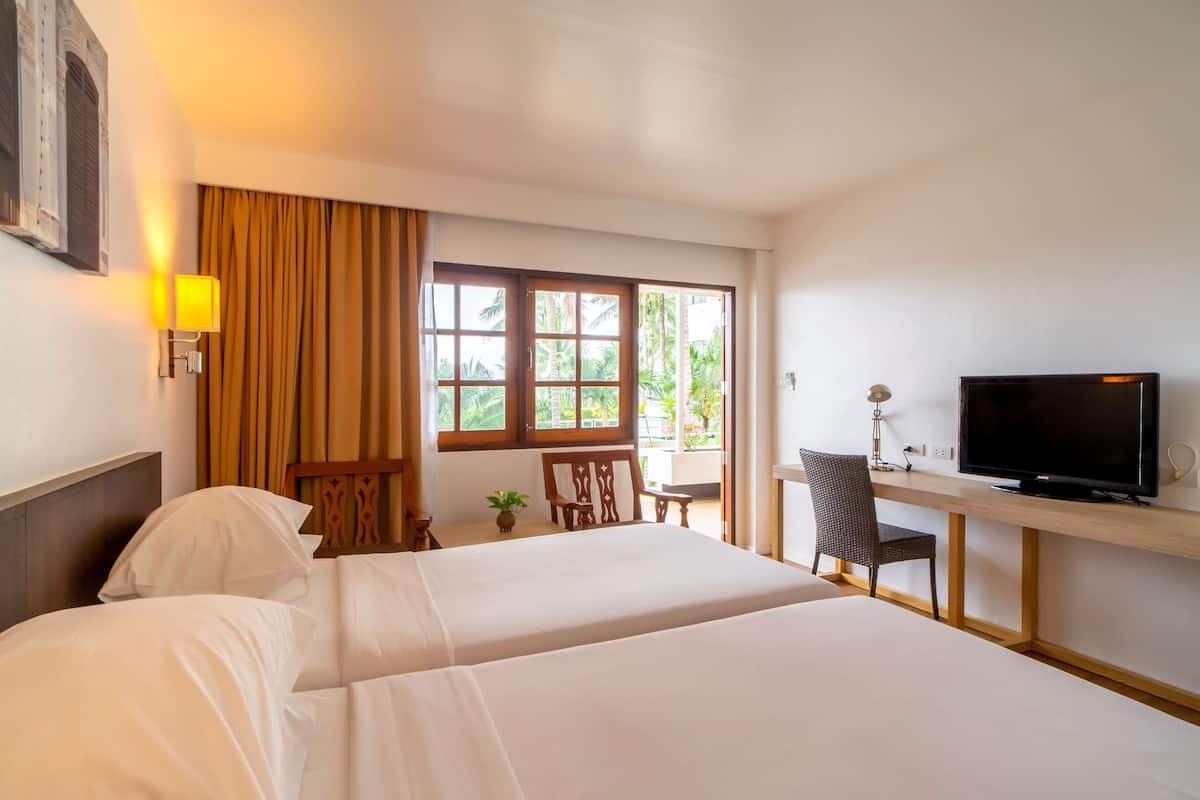 Habitación de hotel con dos camas, un escritorio con televisor y una ventana con cortinas.