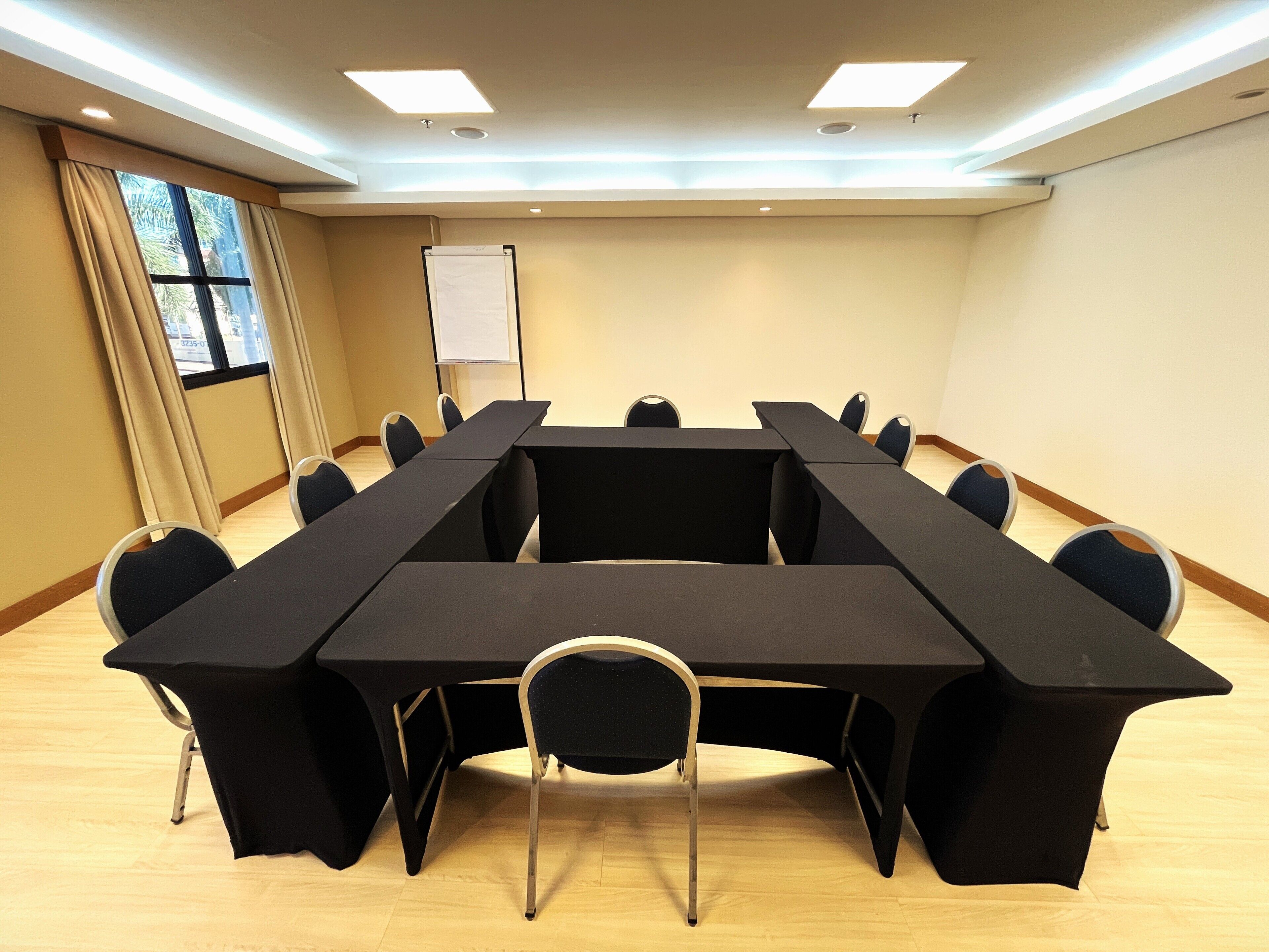 A conference room with a long table and chairs, a whiteboard, and a window with curtains.