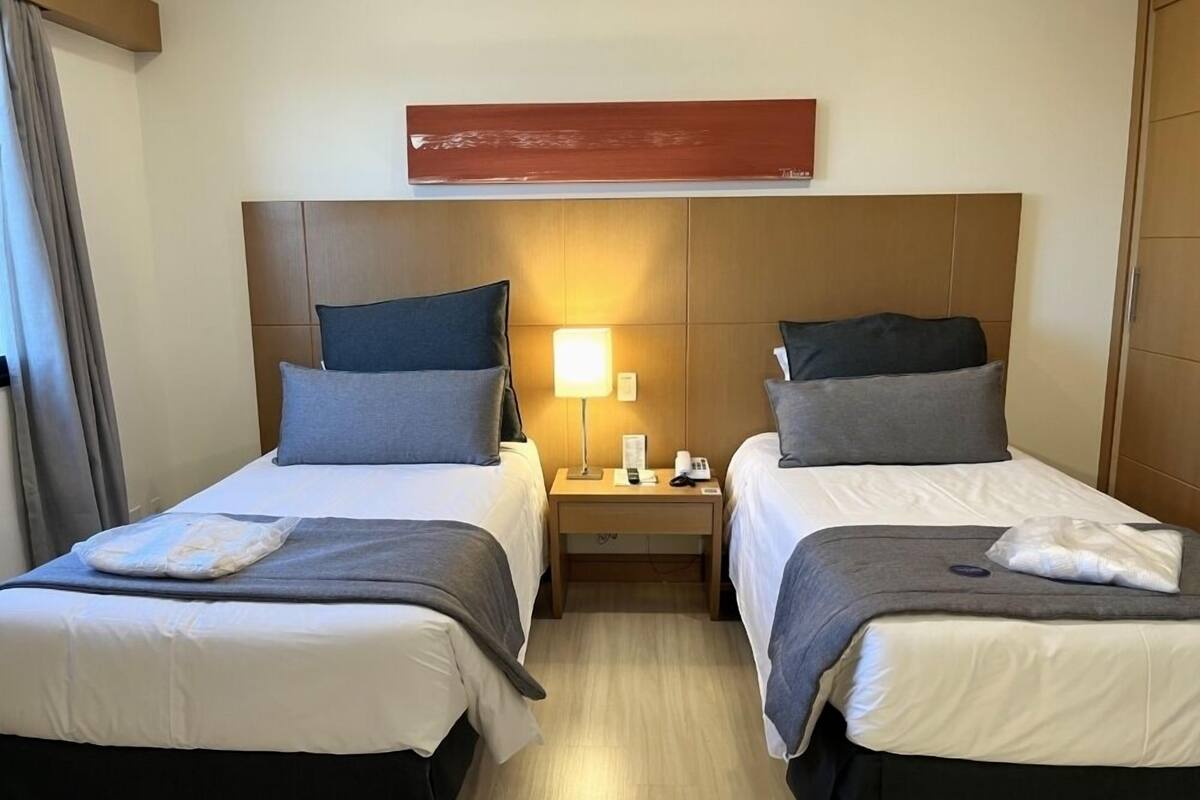 Een hotelkamer met twee bedden, elk voorzien van een kussen en een deken. Daartussen bevindt zich een nachtkastje met een lamp en een telefoon.