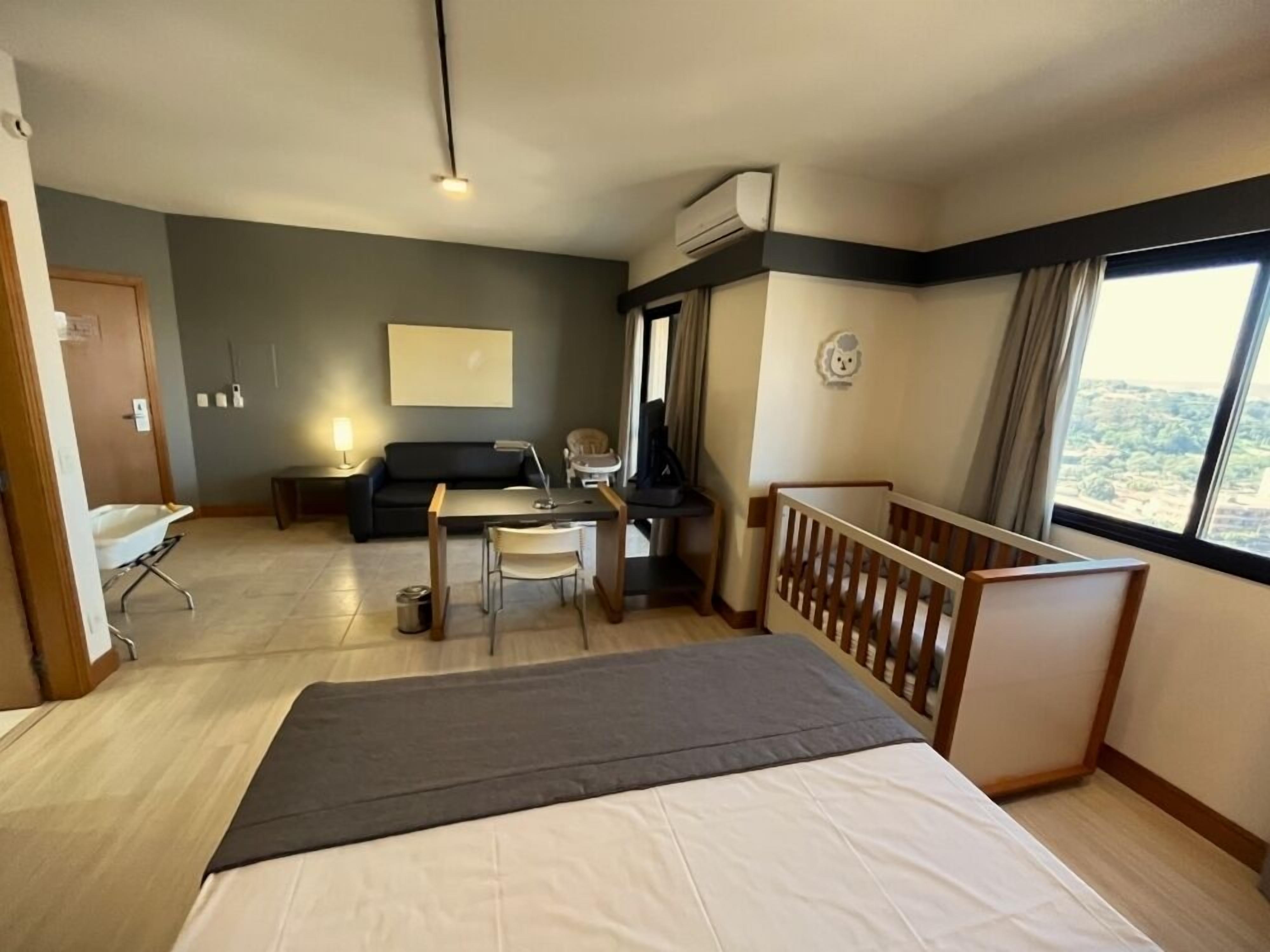 A hotel room with a bed, desk, chair, and a view of the outdoors.