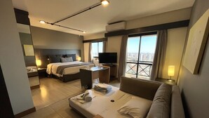 Habitación de hotel con cama, sofá, escritorio, televisión y balcón con vistas a la ciudad.