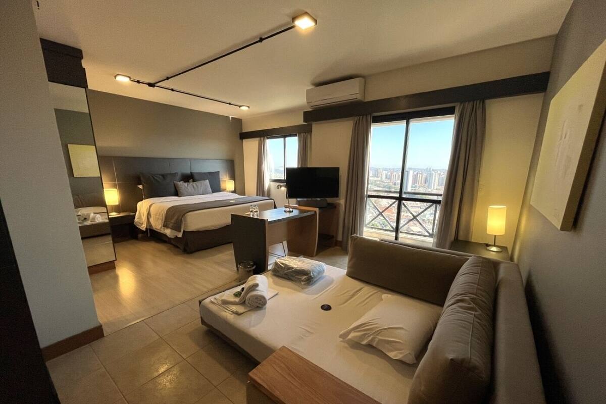 Een hotelkamer met een bed, een bank, een bureau, een televisie en een balkon met uitzicht op de stad.