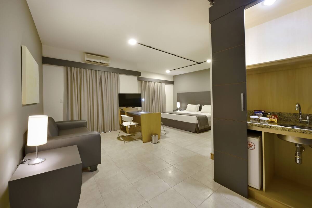 Een moderne hotelkamer met een bank, bureau, bed en kitchenette.