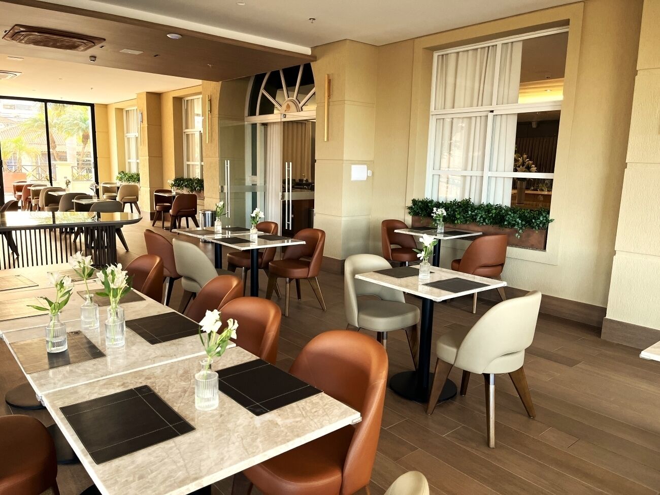 A modern restaurant with multiple tables and chairs, some with vases of flowers.