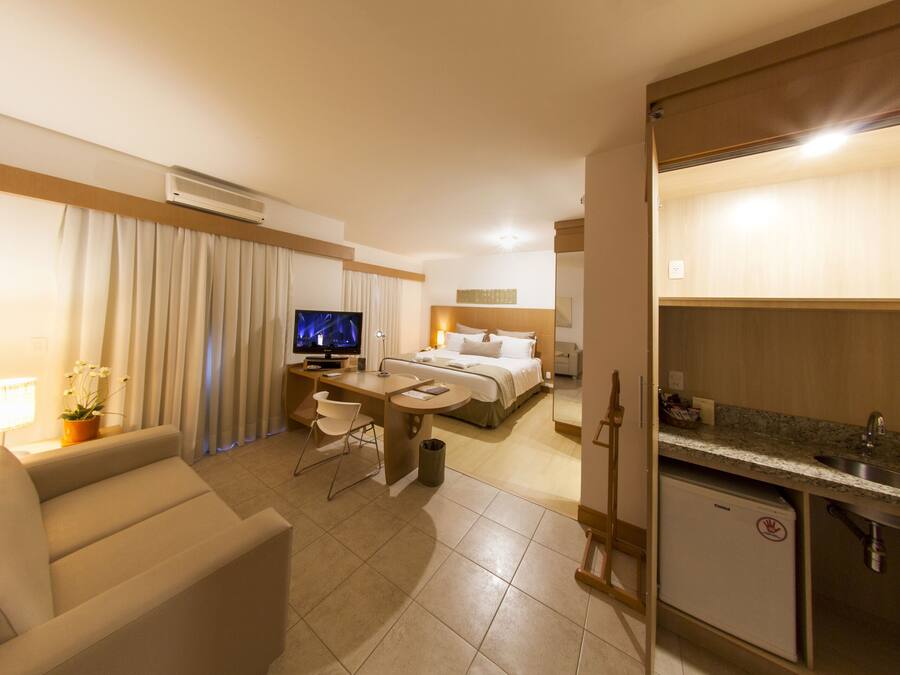 A hotel room with a bed, a desk, a TV, a small kitchenette, and a sofa.