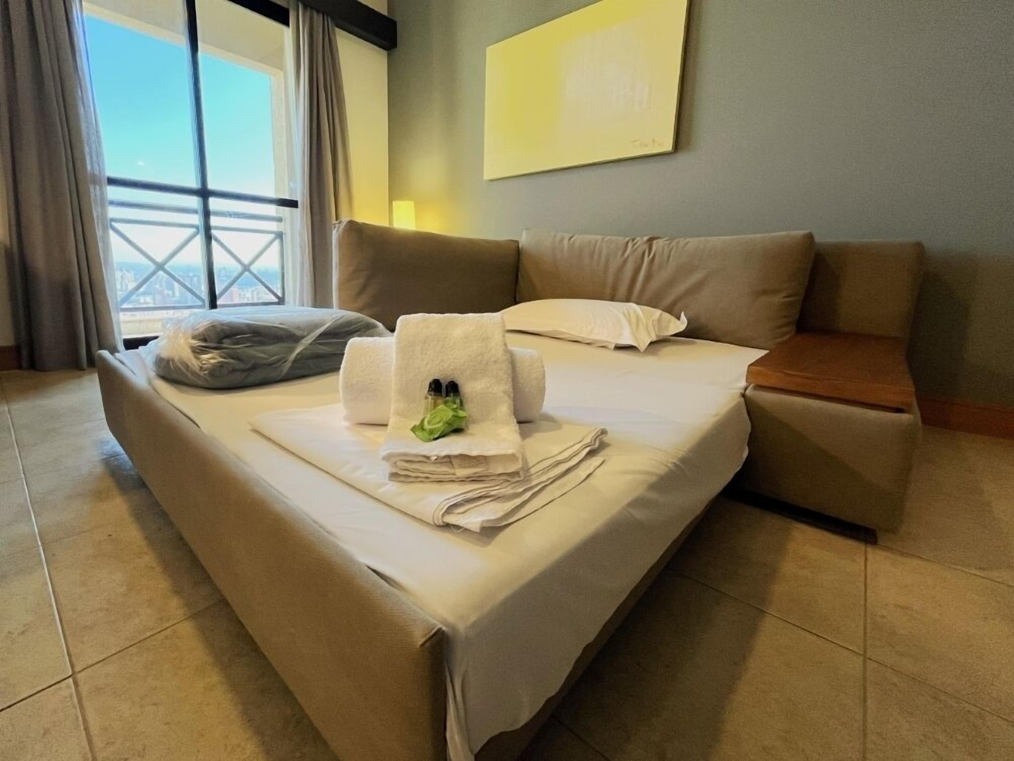 Cama bem arrumada com toalhas e amenities, um sofá e uma janela com cortinas.