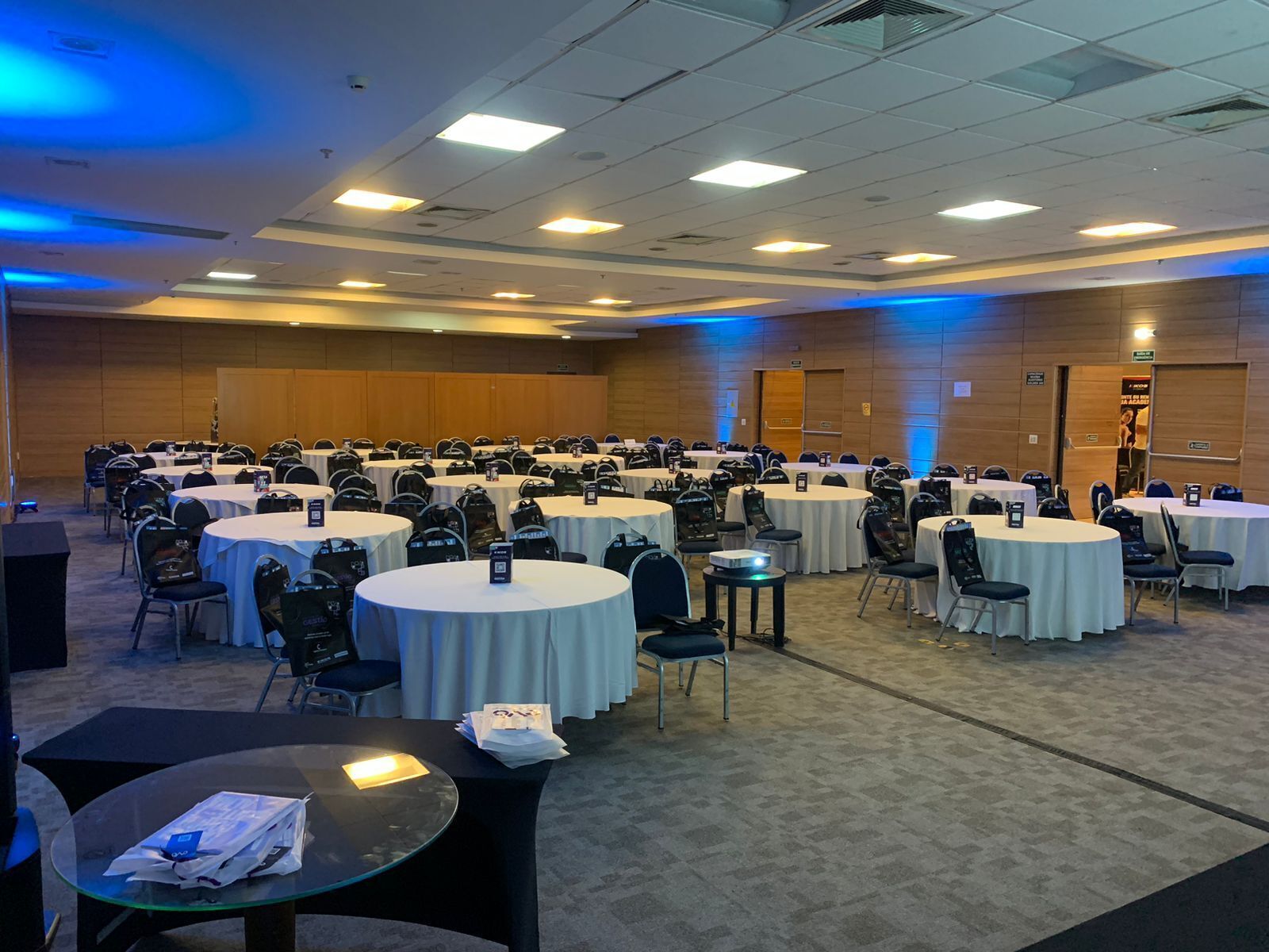 A conference room with multiple round tables and chairs, equipped with nameplates and bags.