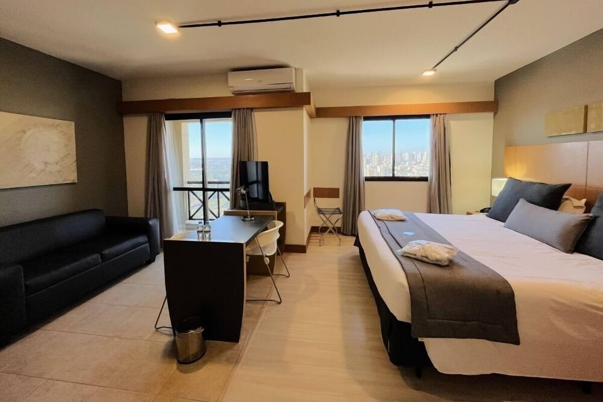 Een hotelkamer met een bed, een bureau, een stoel, een televisie en uitzicht op de stad.