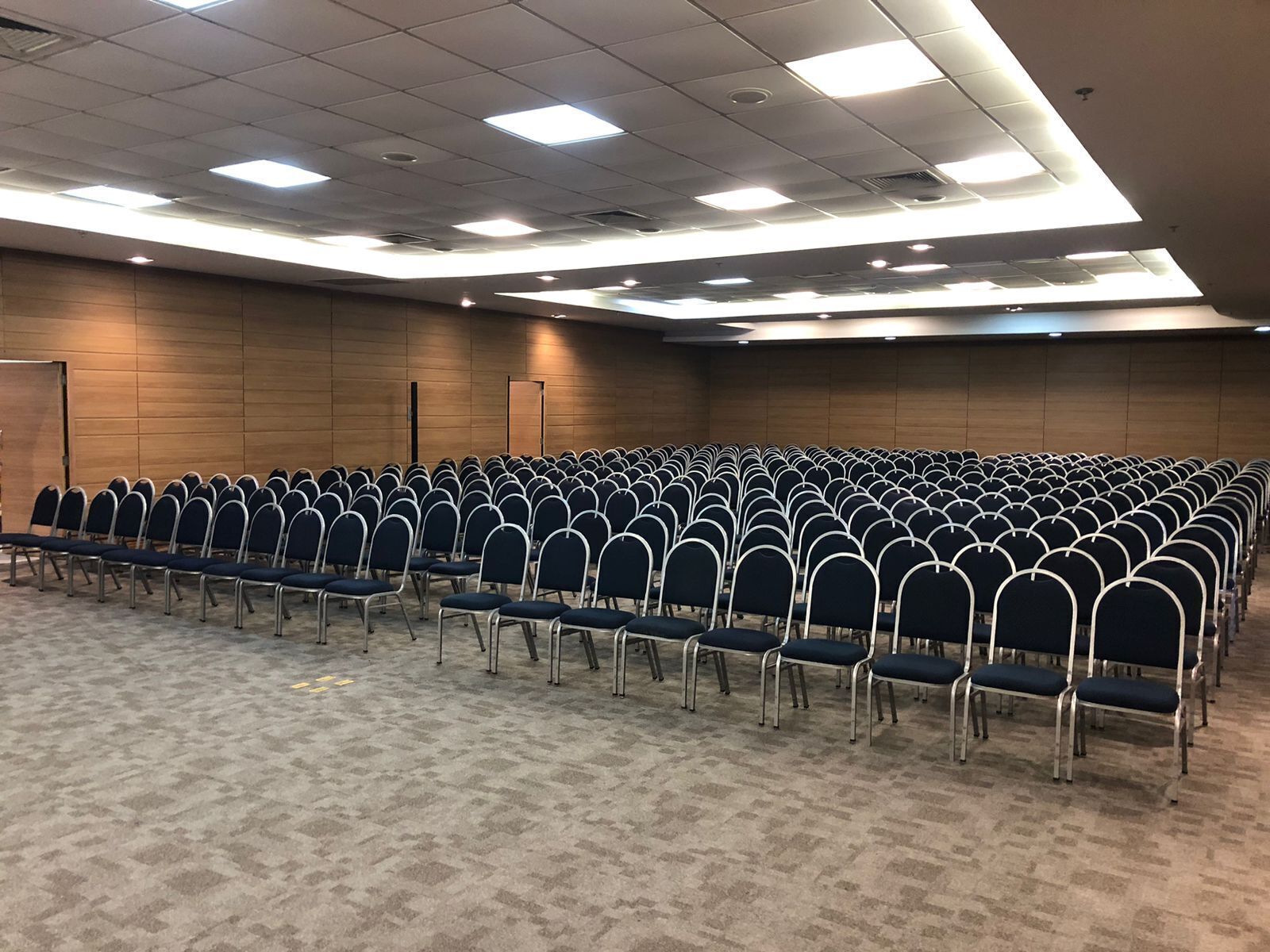 A conference room with rows of chairs, carpeted floor, and ceiling lights.