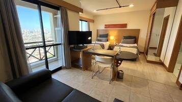 Een hotelkamer met een bank, een eettafel, een televisie, twee bedden en uitzicht op de stad.