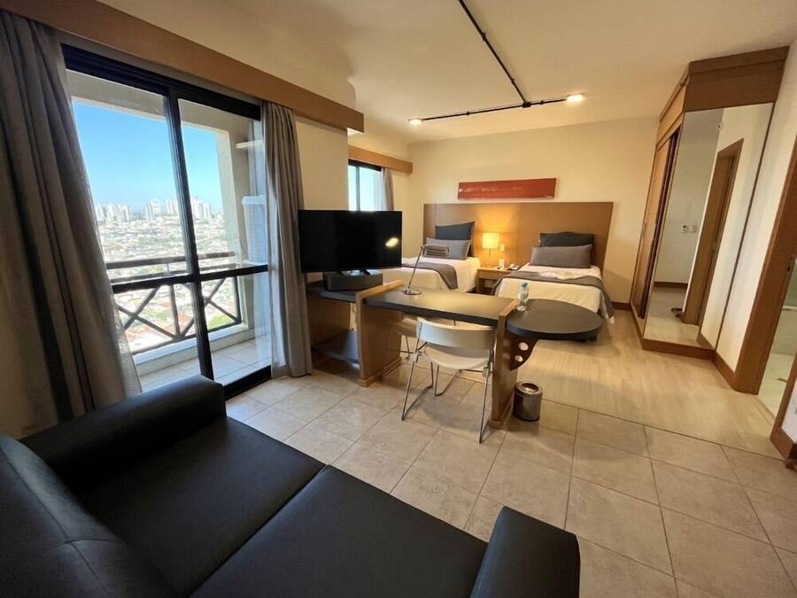Een hotelkamer met een bank, een eettafel, een televisie, twee bedden en uitzicht op de stad.
