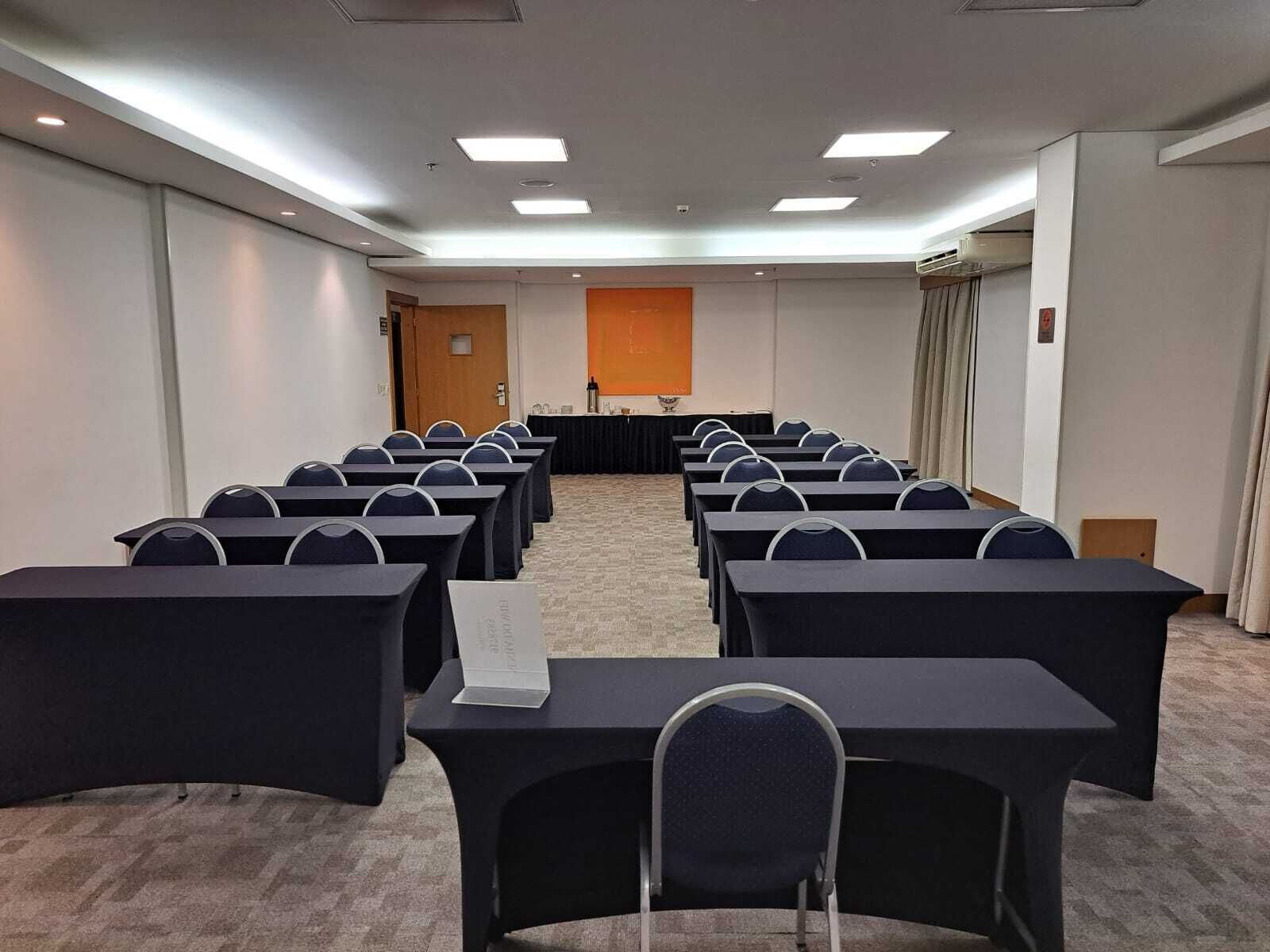 A conference room with rows of tables and chairs, a podium, and a projector screen.