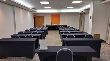 A conference room with rows of tables and chairs, a podium, and a projector screen.