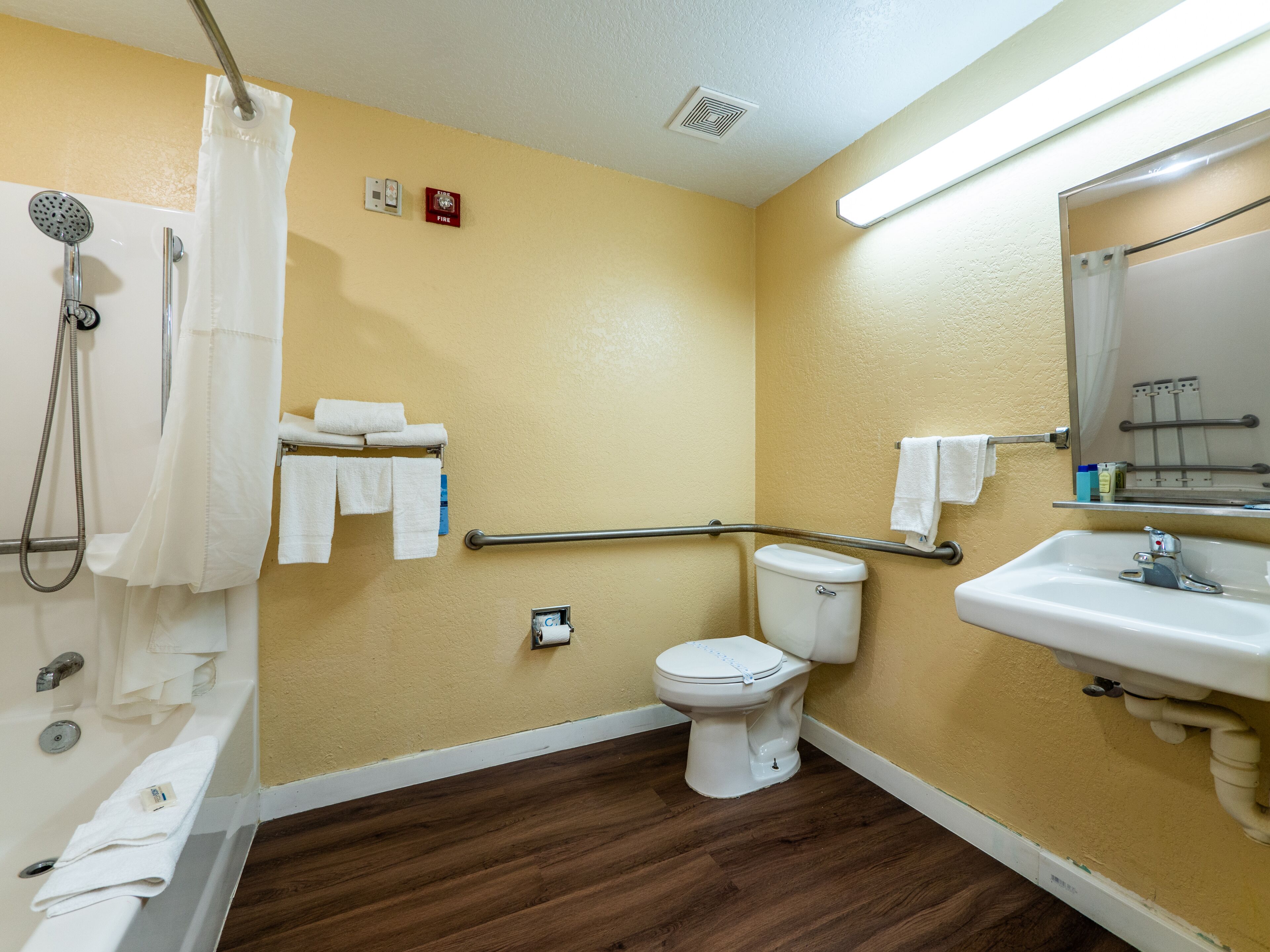 A bathroom with a toilet, sink, shower, and handrails.