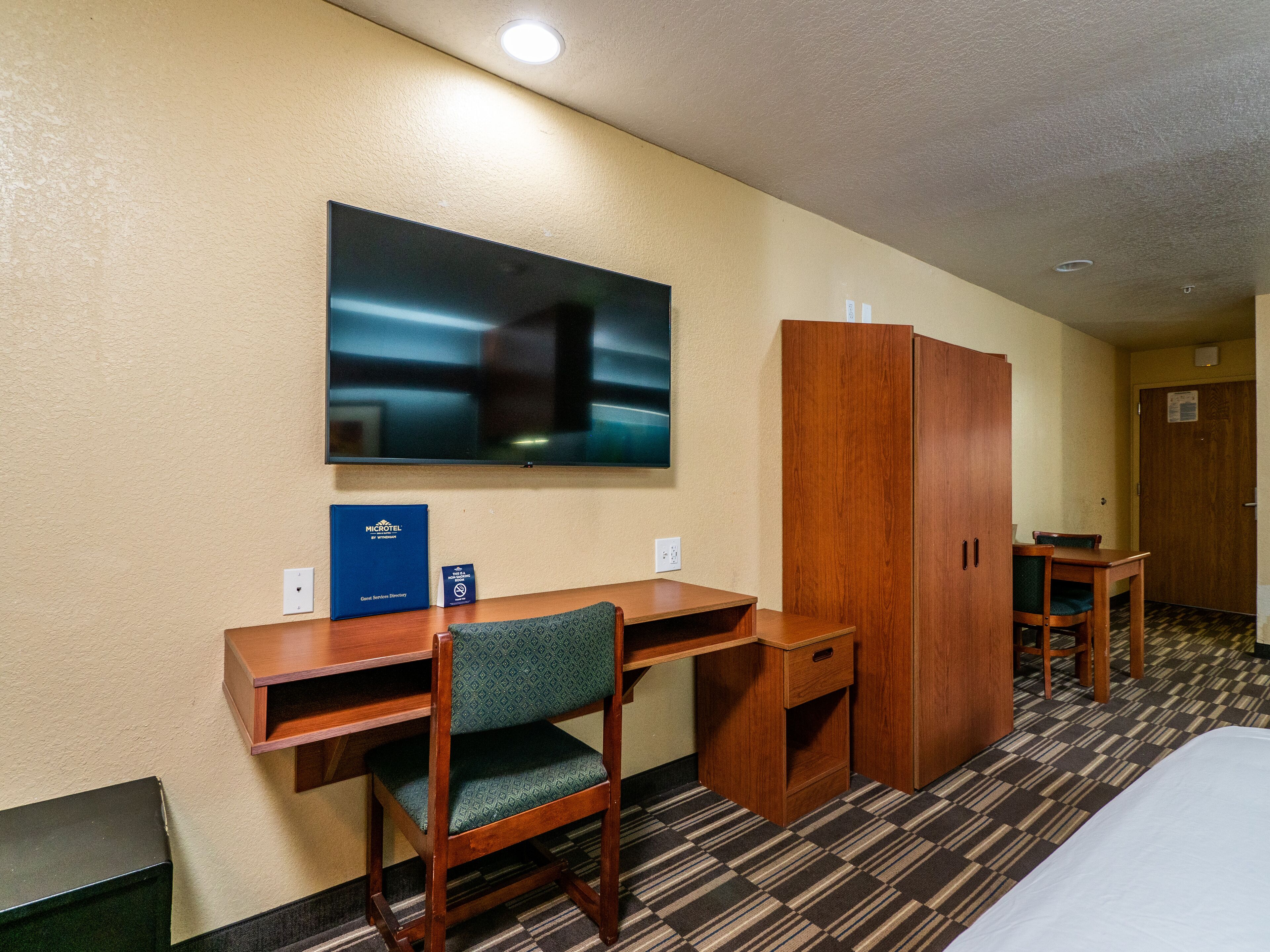 Una habitación de hotel con cama, escritorio, silla, armario, televisor y una mesita.