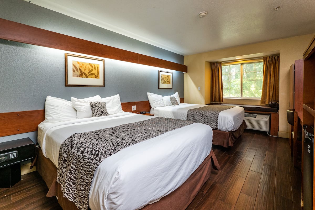 A hotel room with two beds, a window with curtains, a heater, and artwork on the walls.